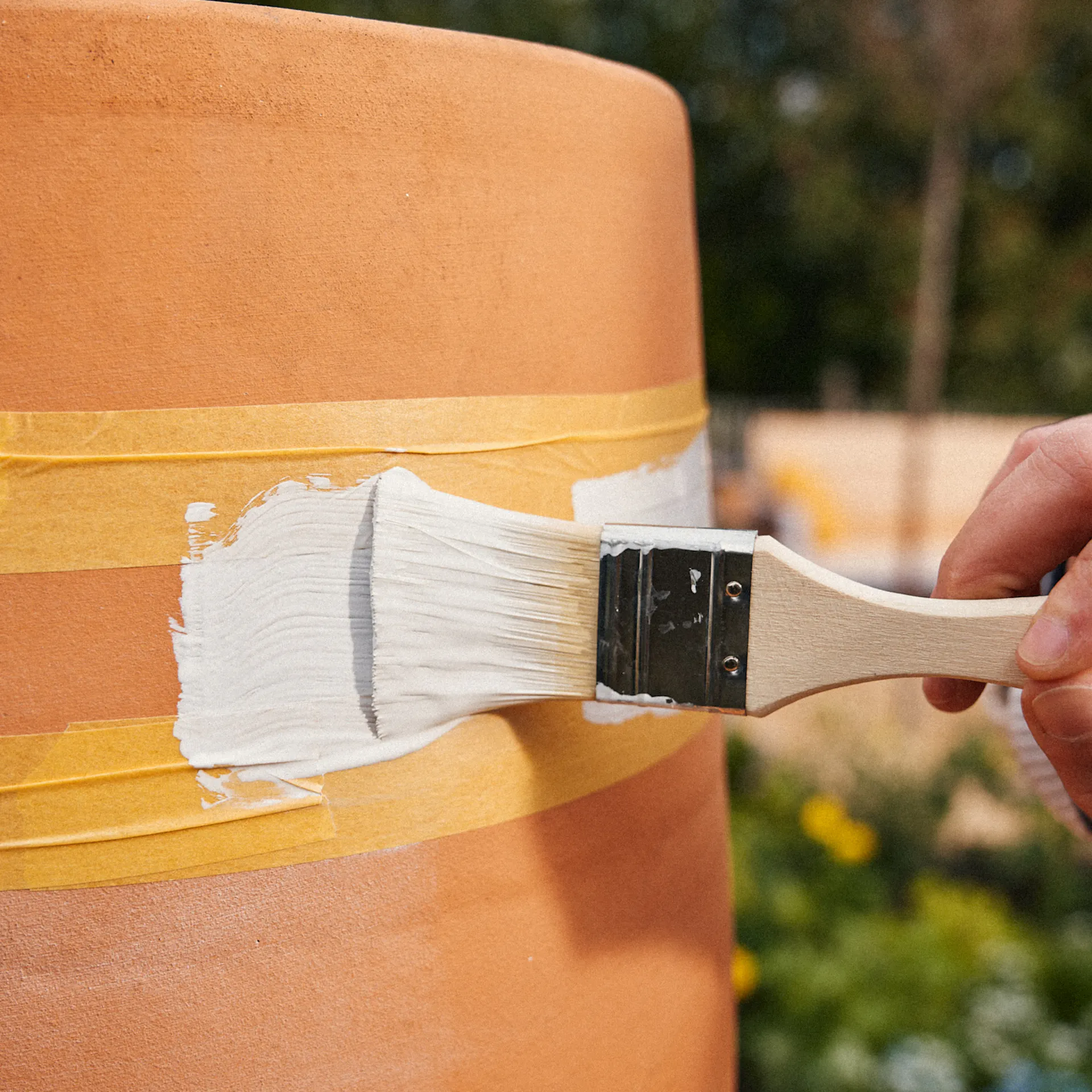 Egy nő festi a terrakotta cserepet fehér festékkel.