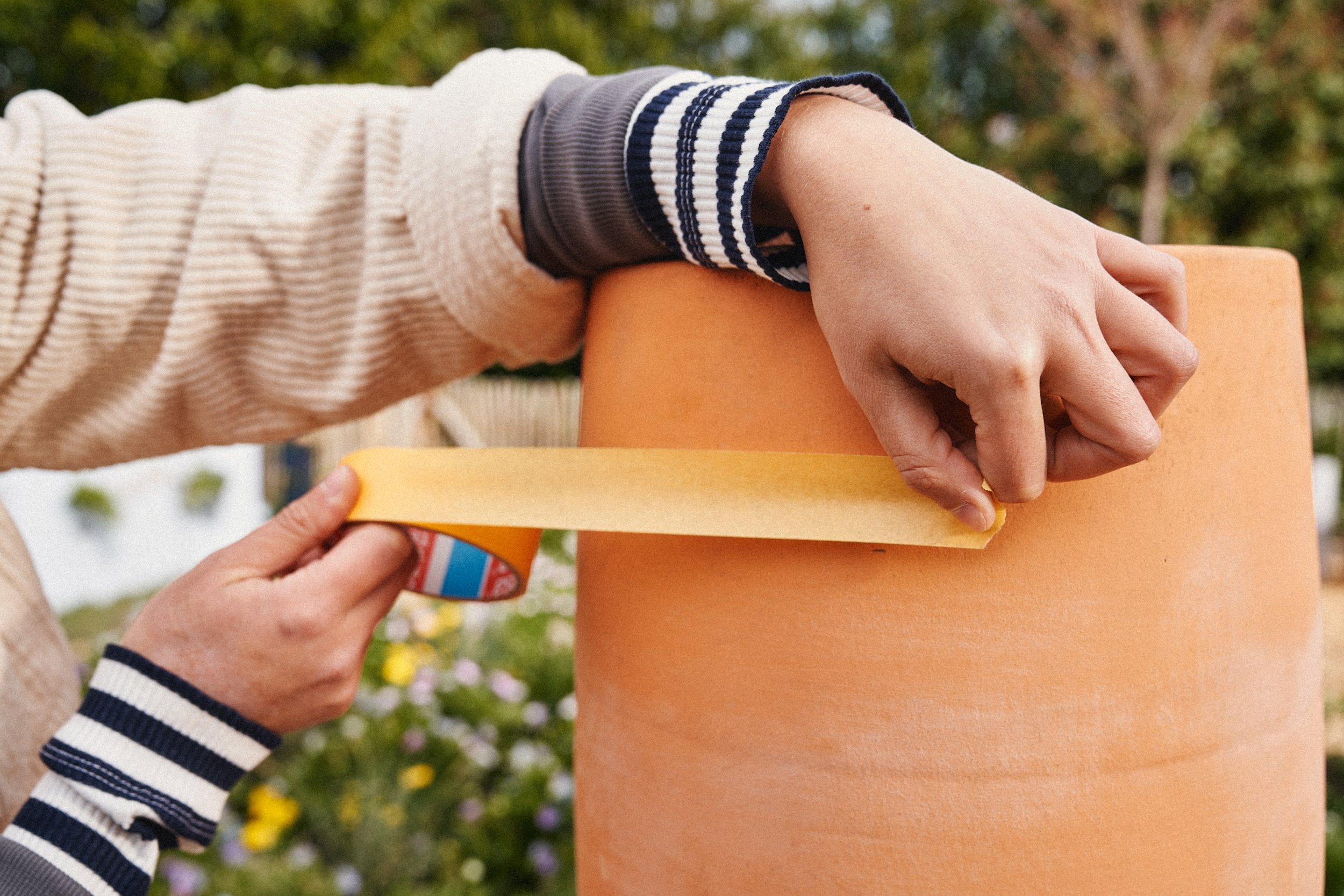 Egy nő maszkolószalagot ragaszt egy terrakotta edényre.