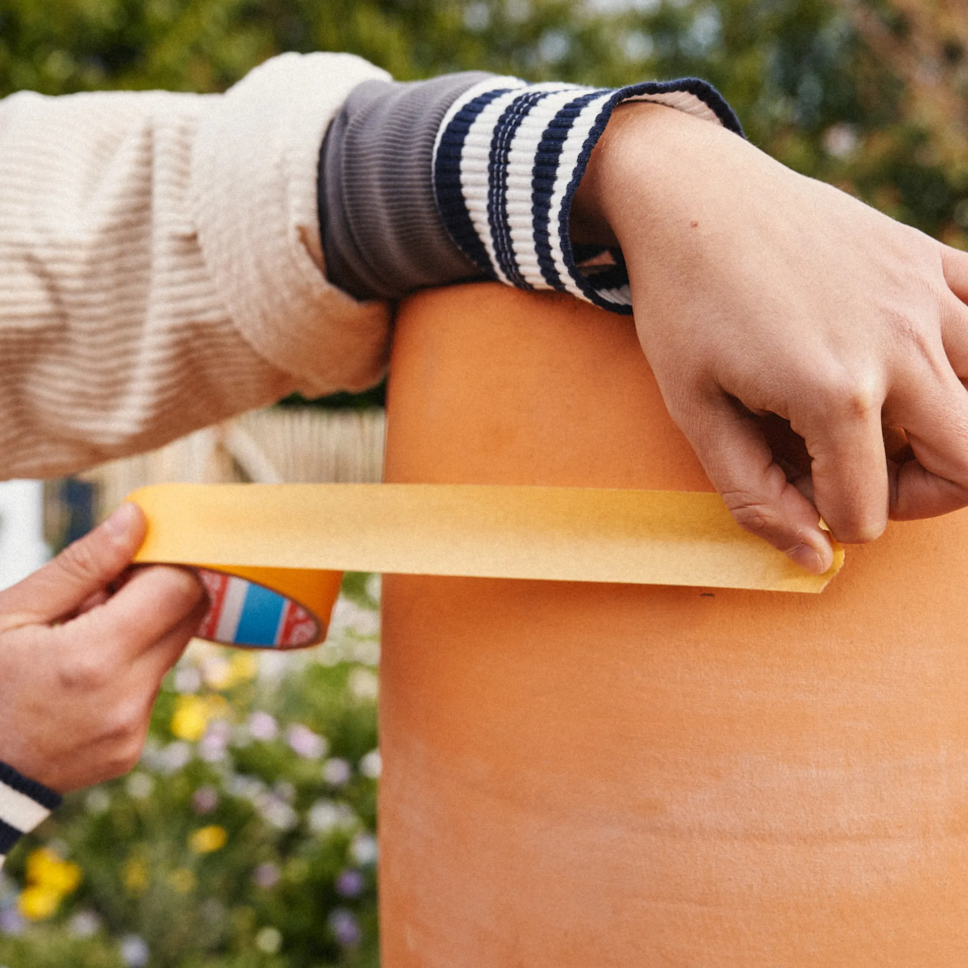 Egy nő maszkolószalagot ragaszt egy terrakotta edényre.