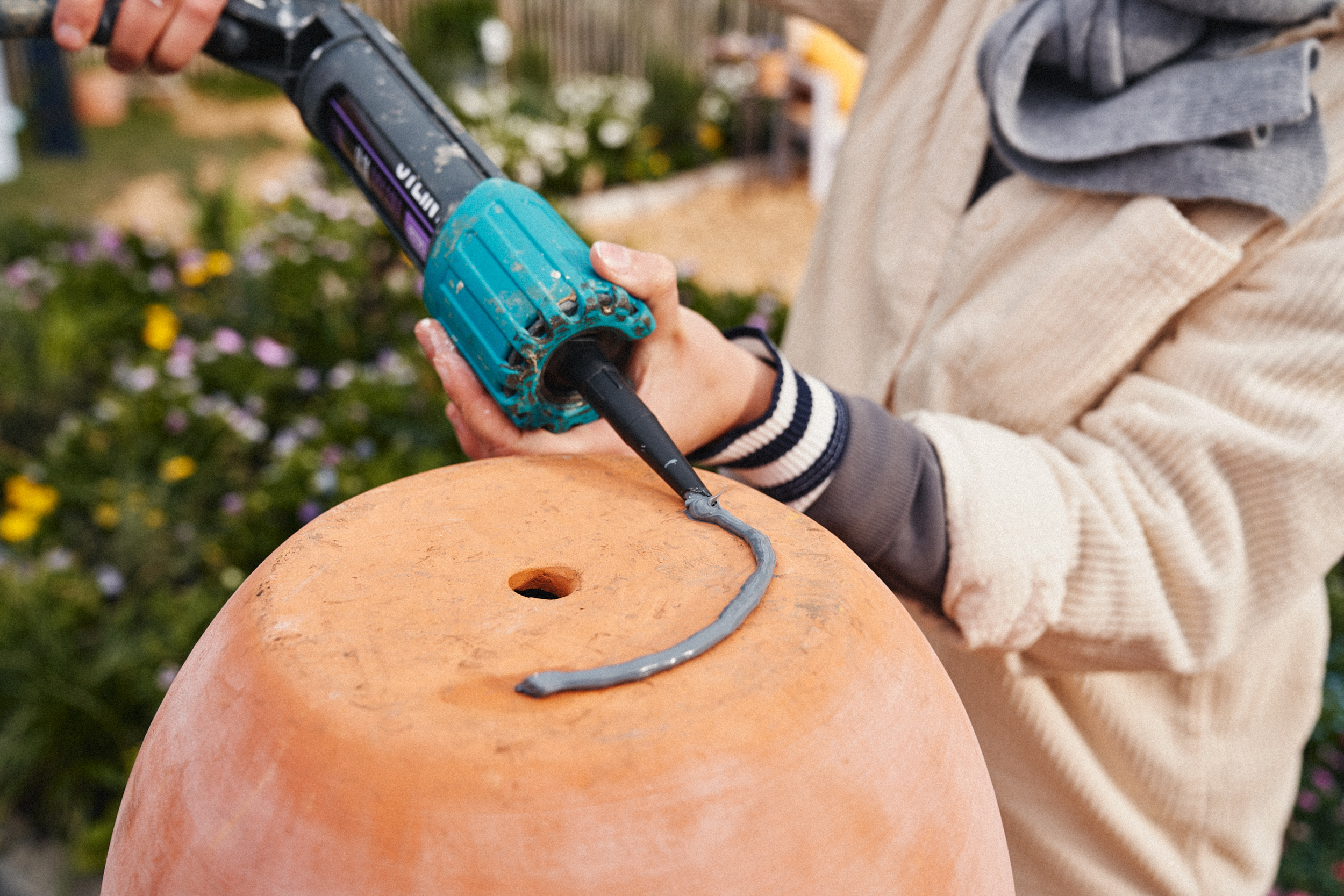 A nő egy tömítő pisztollyal felhordja a szerelési ragasztót a terrakotta edény aljára.