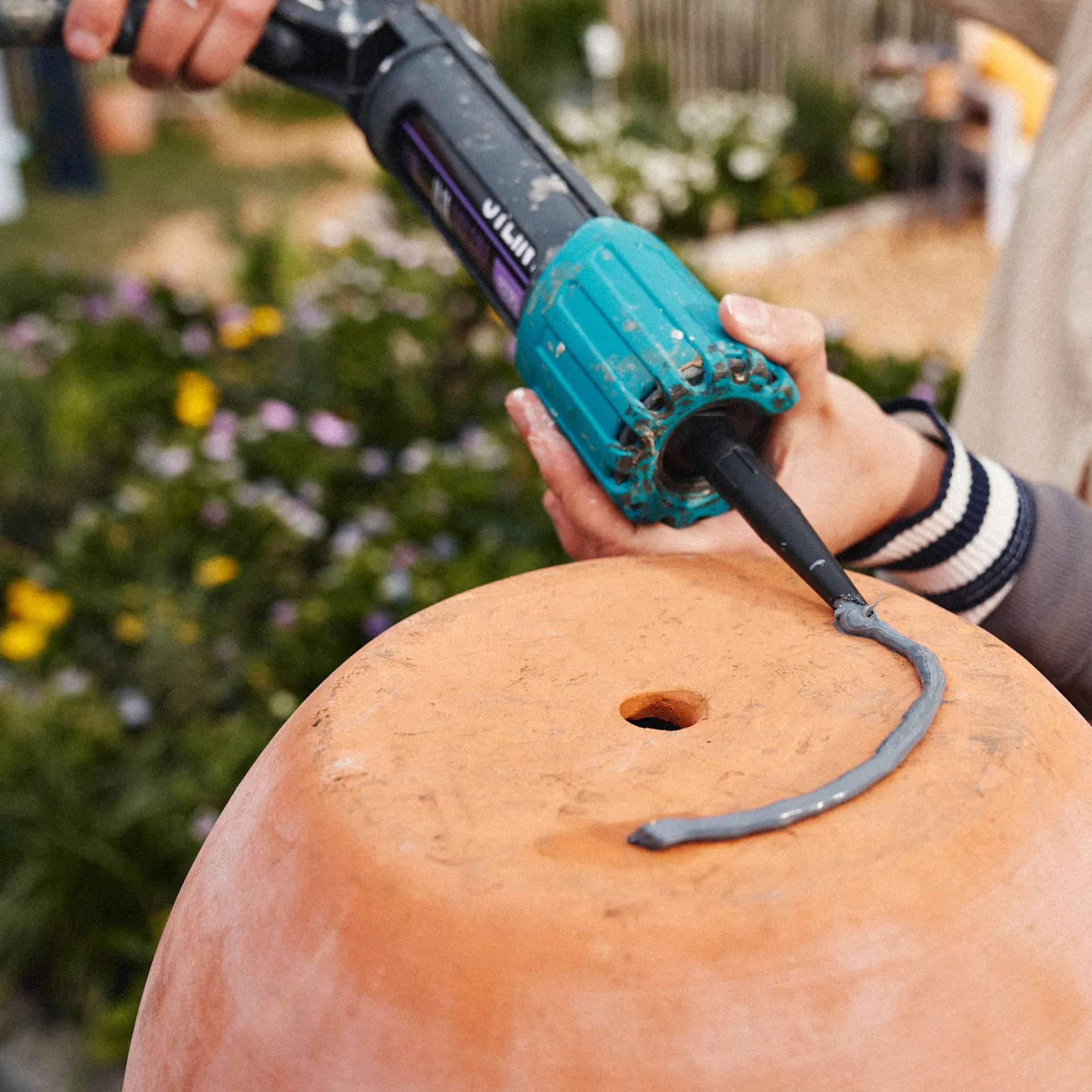 A nő egy tömítő pisztollyal felhordja a szerelési ragasztót a terrakotta edény aljára.