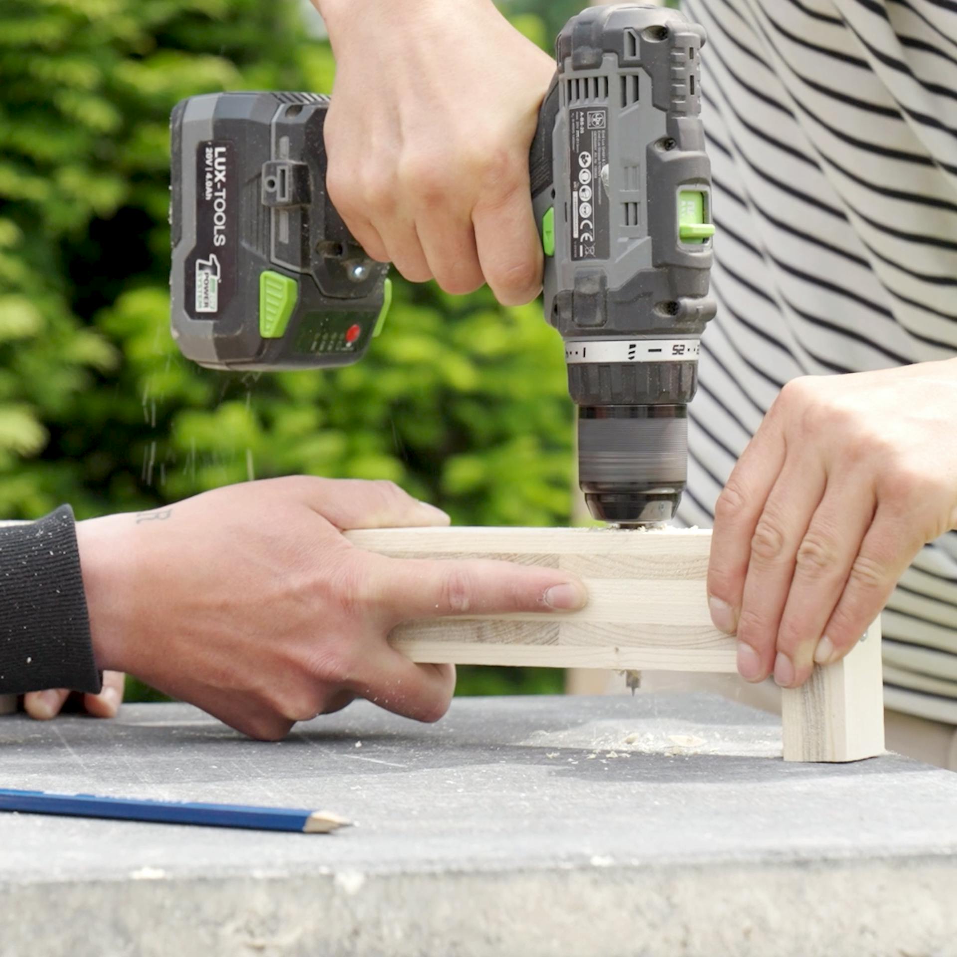 Ein Handwerker hält ein Kantholz fest und der andere bohrt dort an der Seite ein Loch hinein.