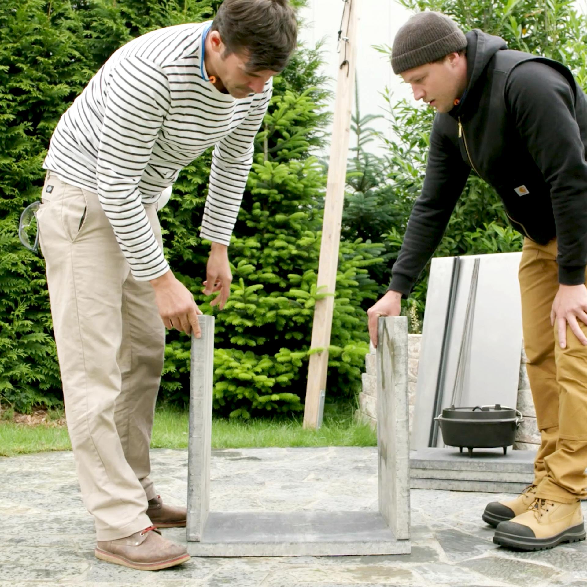 Zwei Handwerker stellen den Rahmen der Platten für einen Grilltisch zusammen und halten die Seitenteile fest.
