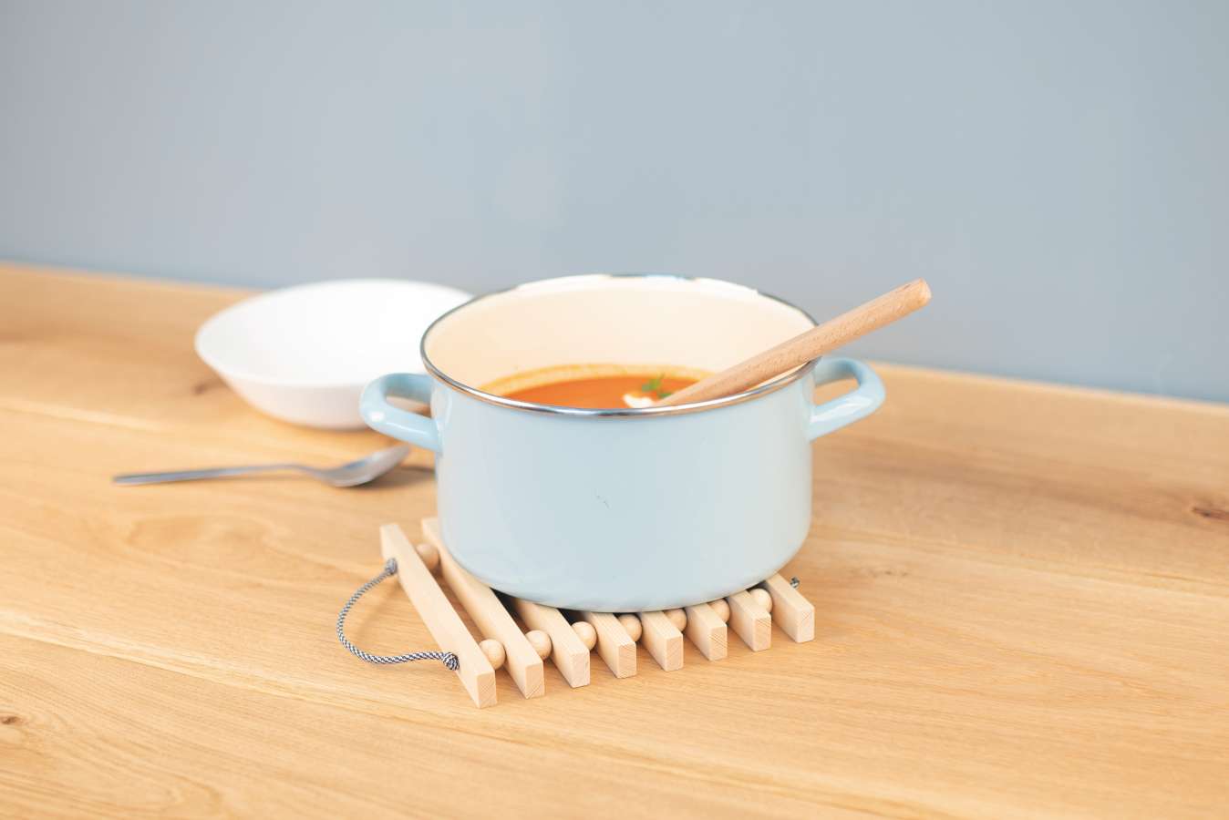 Auf einem Leistenuntersetzer steht einer kleiner, hellblauer Topf, in dem Suppe ist