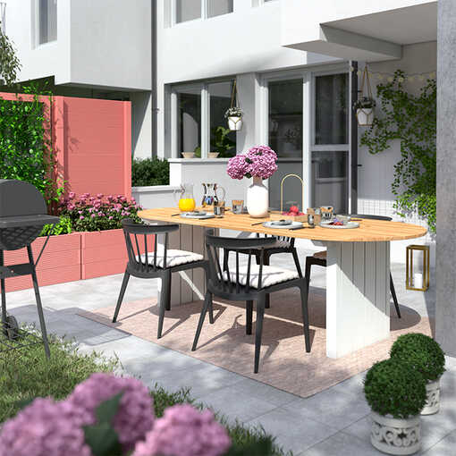 Gartentisch Emilia steht auf einer hellen Terrasse, wo das Hochbeet Alfred in einem pastellrot als Sichschutz aufgestellt worden ist.