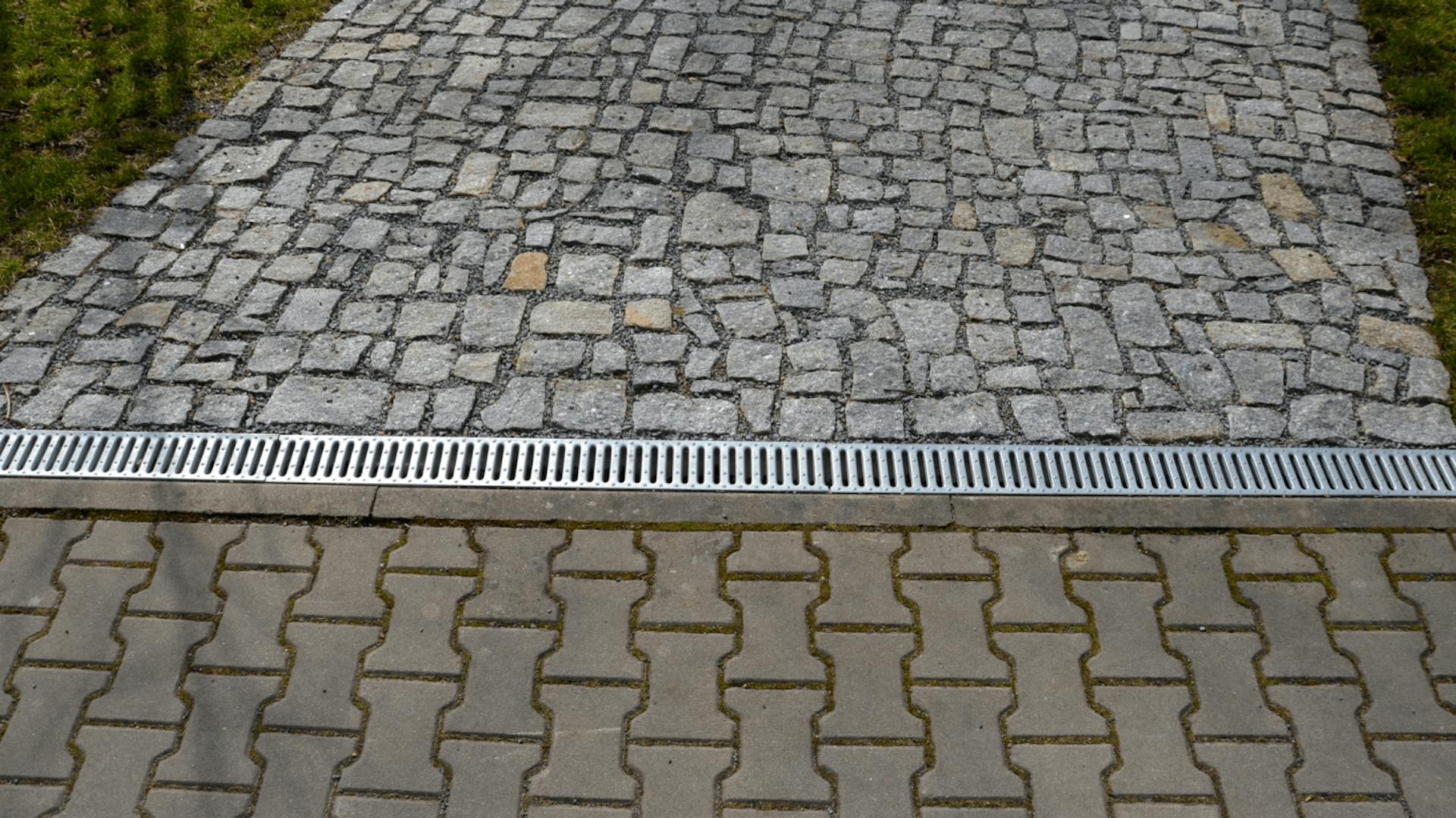 Entwässerungsrinne zwischen zwei Wegen aus Pflastersteinen.
