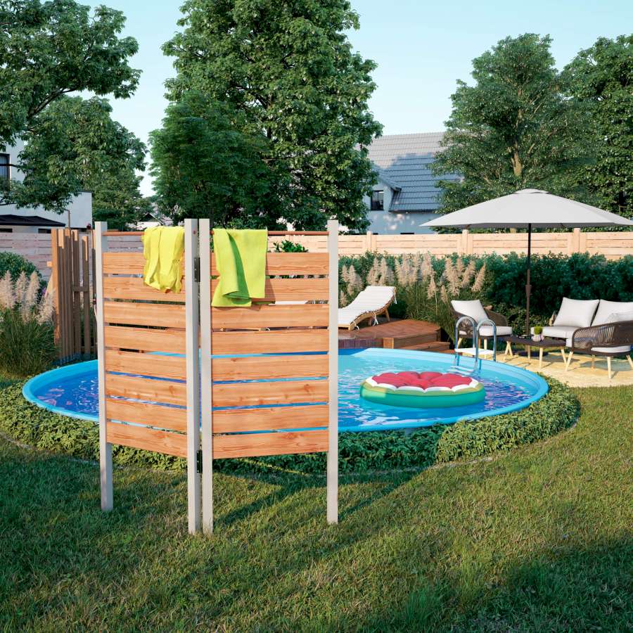 Ein selbstgebauter Raumtrenner steht in einem Garten vor einem Pool. Auf dem Raumtrenner liegen Handtücher.