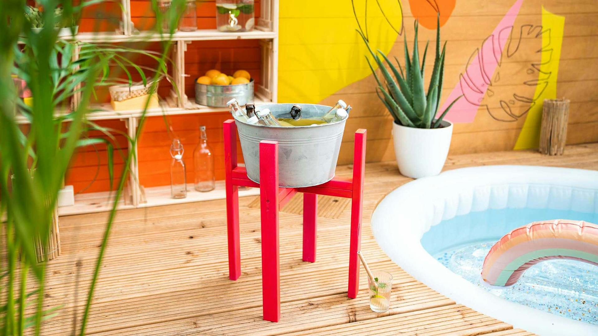 Die selbstgemachte Getränkekühlung steht auf einer Holzterrasse, auf welcher ein Pool eingesetzt worden ist und daneben die Pool Weinkisten platziert sind.