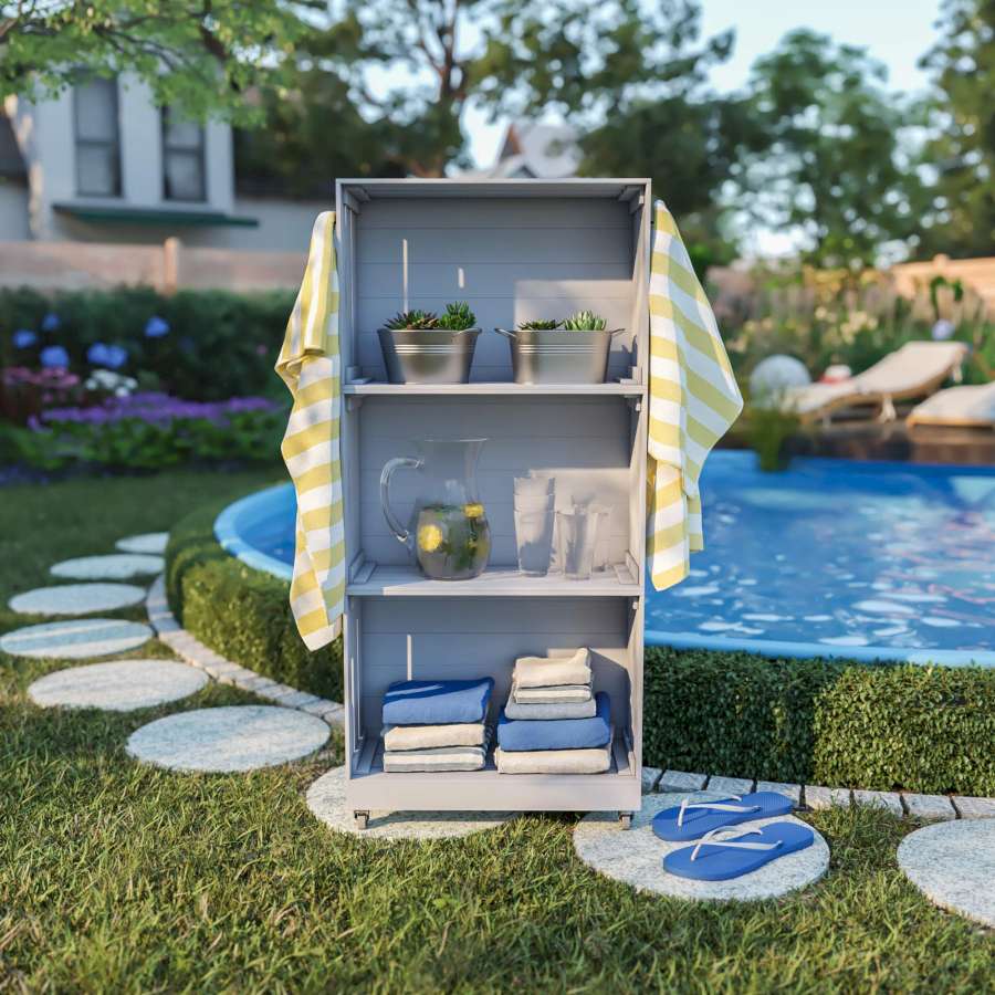 Ein Poolregal aus Weinkisten, in dem sich Pflanzen, eine Wasserkaraffe, Gläser und Handtücher befinden, steht vor einem Pool.