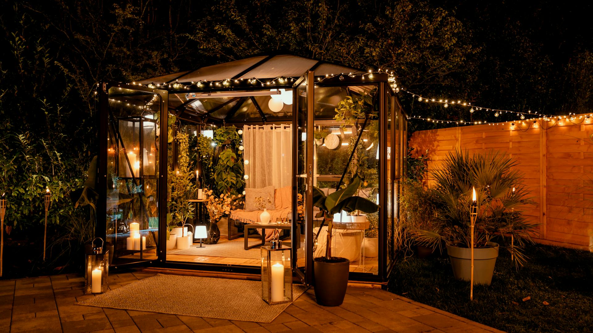 Gartenhaus aus Glas mit vielen Kerzen und Leuchten bei Nacht.