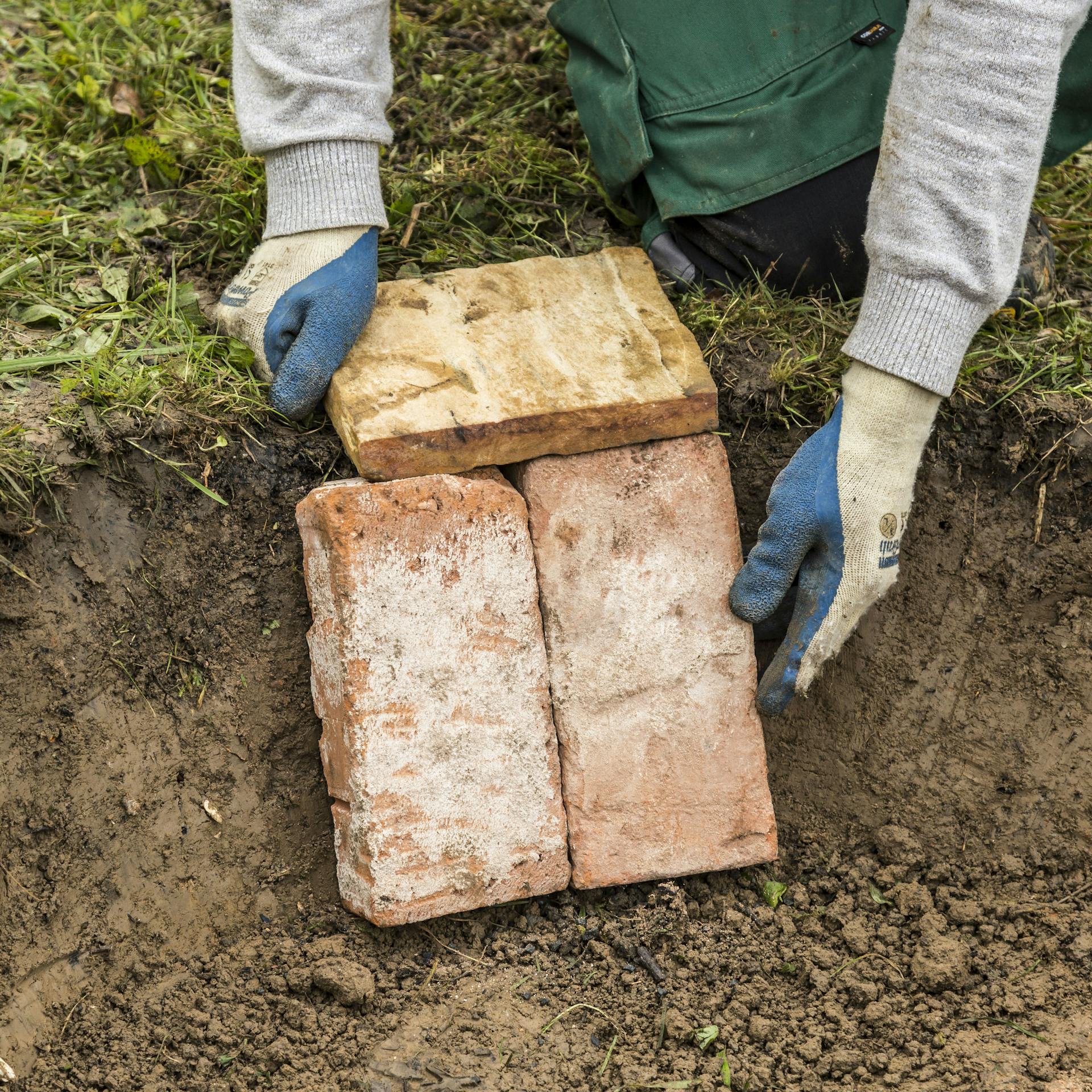Person legt Steine an die Innenwand der Feuerstelle.