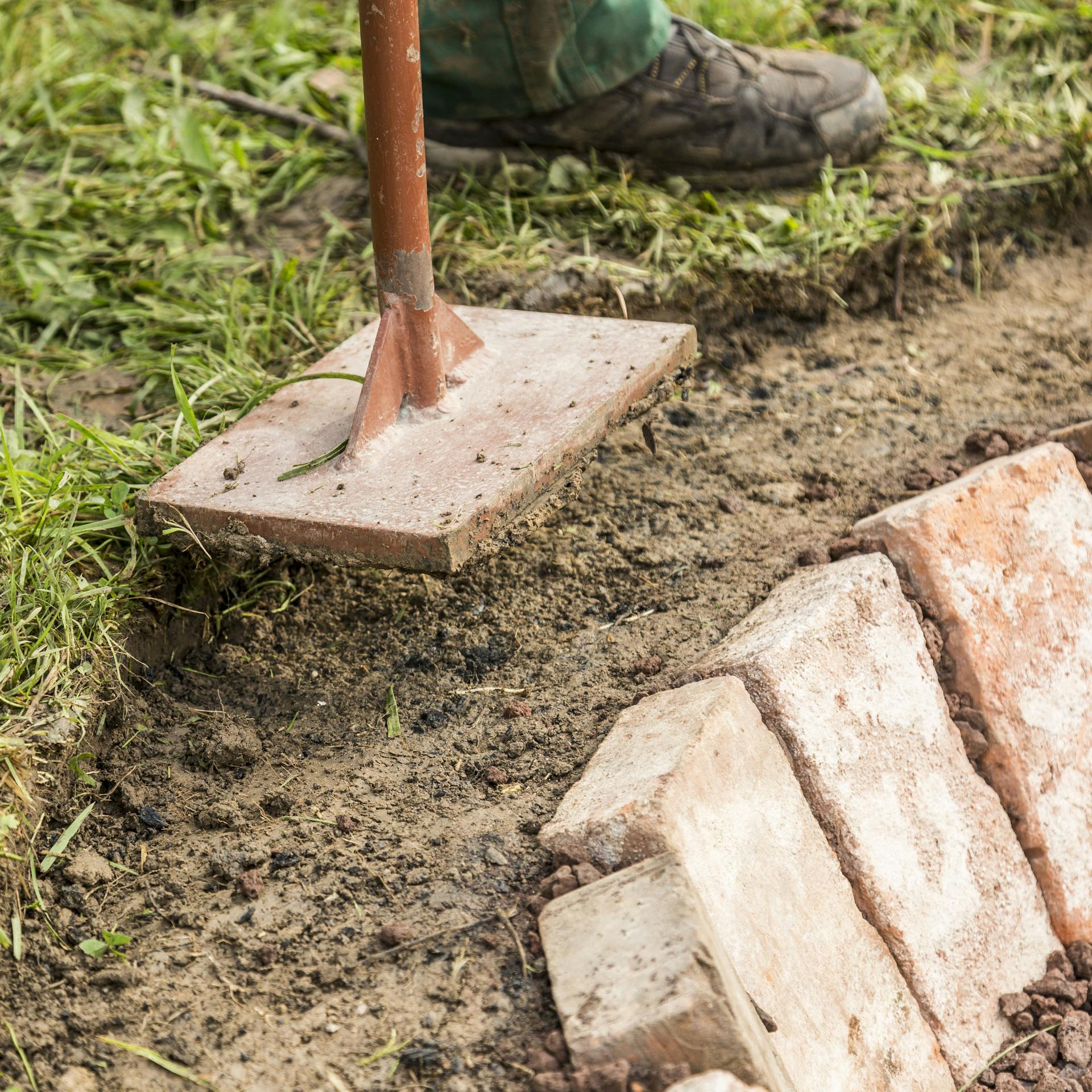 Person verdichtet Rand der Feuerstelle mit Handstampfer.