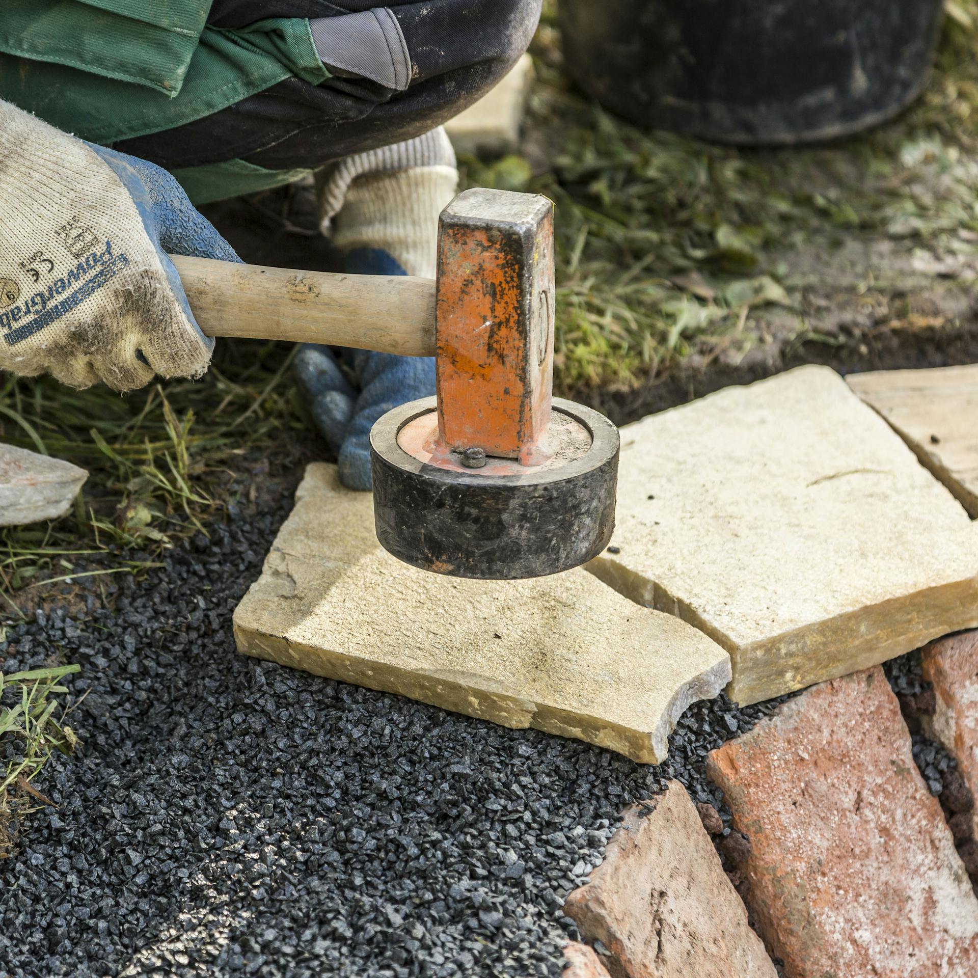 Person klopft Polygonalplatten am Rand der Feuerstelle mit einem Gummihammer fest.