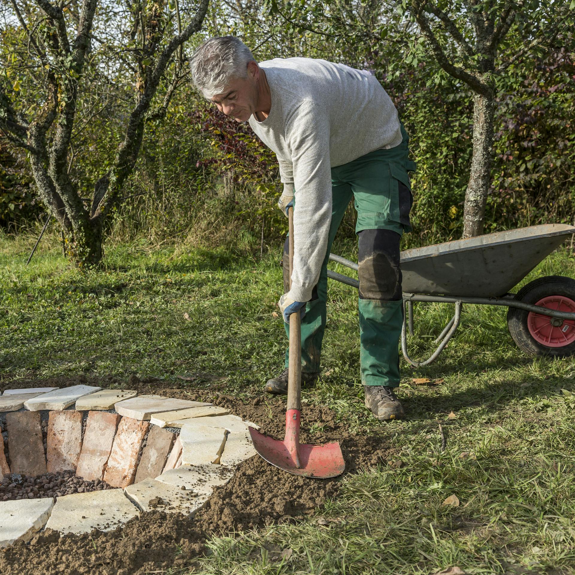 Heimwerker füllt Rand zwischen Feuerstelle und Rasen mit Erde auf.