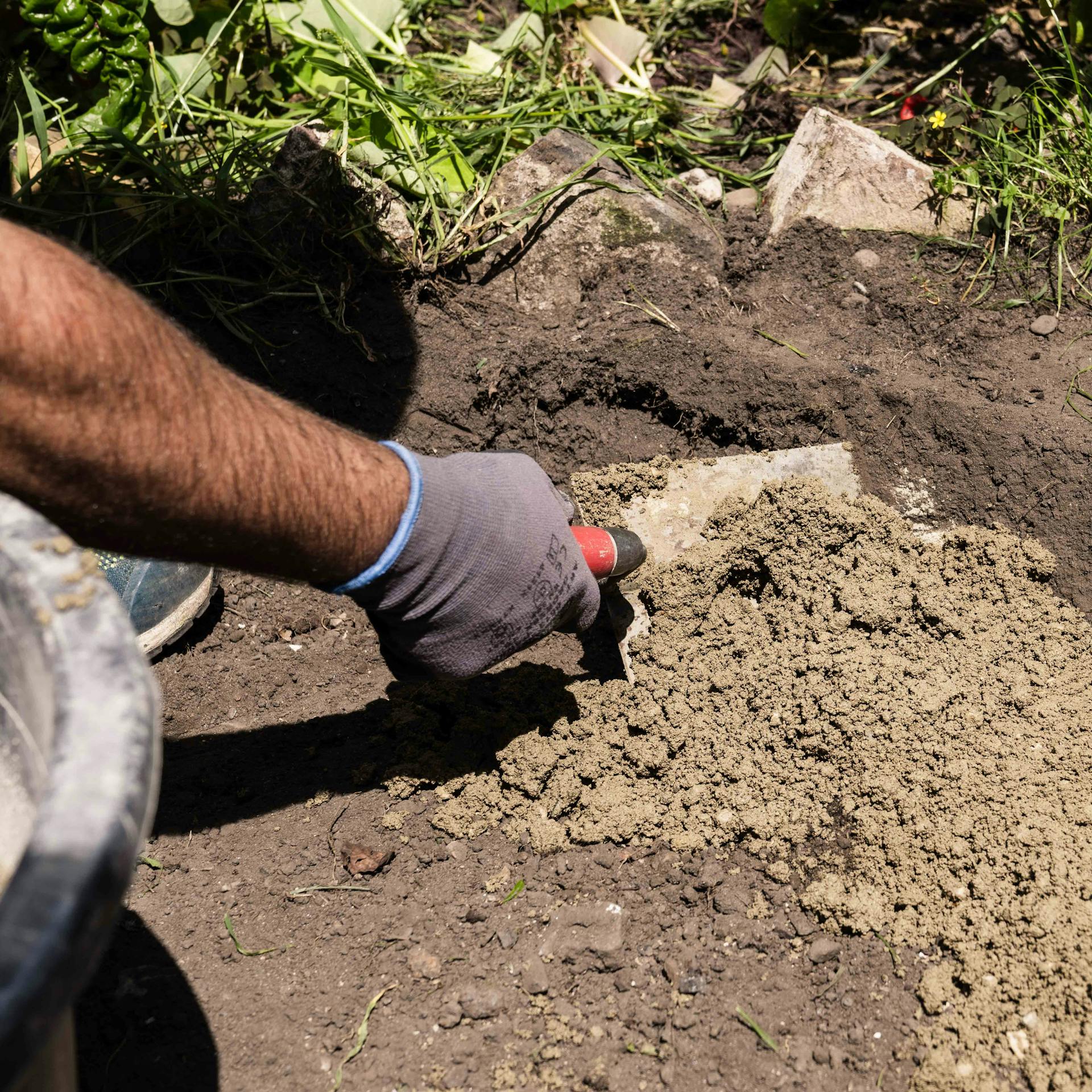 Un hobbista leviga il calcestruzzo nello scavo per braciere con cazzuola.