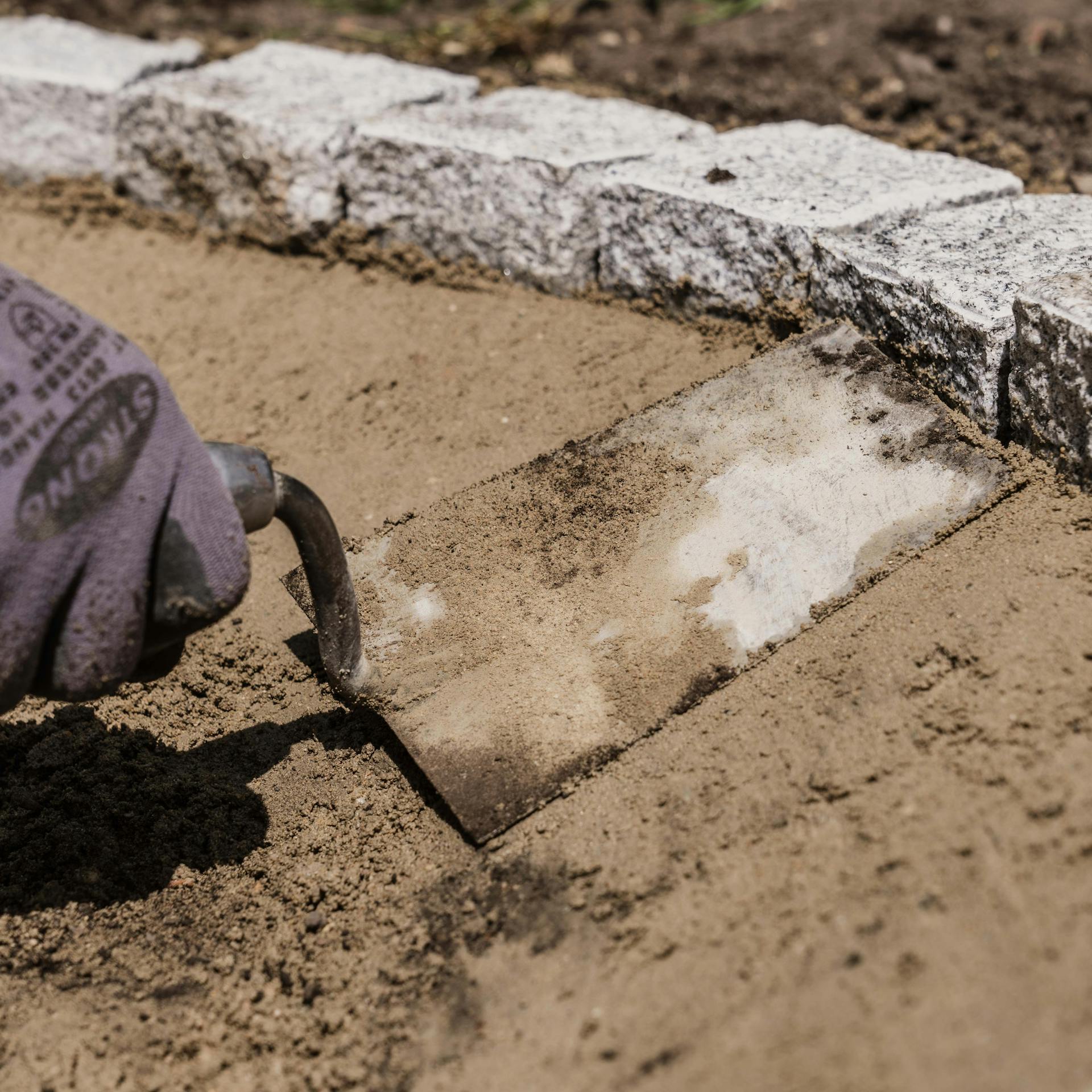 Un hobbista leviga i pezzi posteriori di calcestruzzo per la bordatura della pavimentazione.