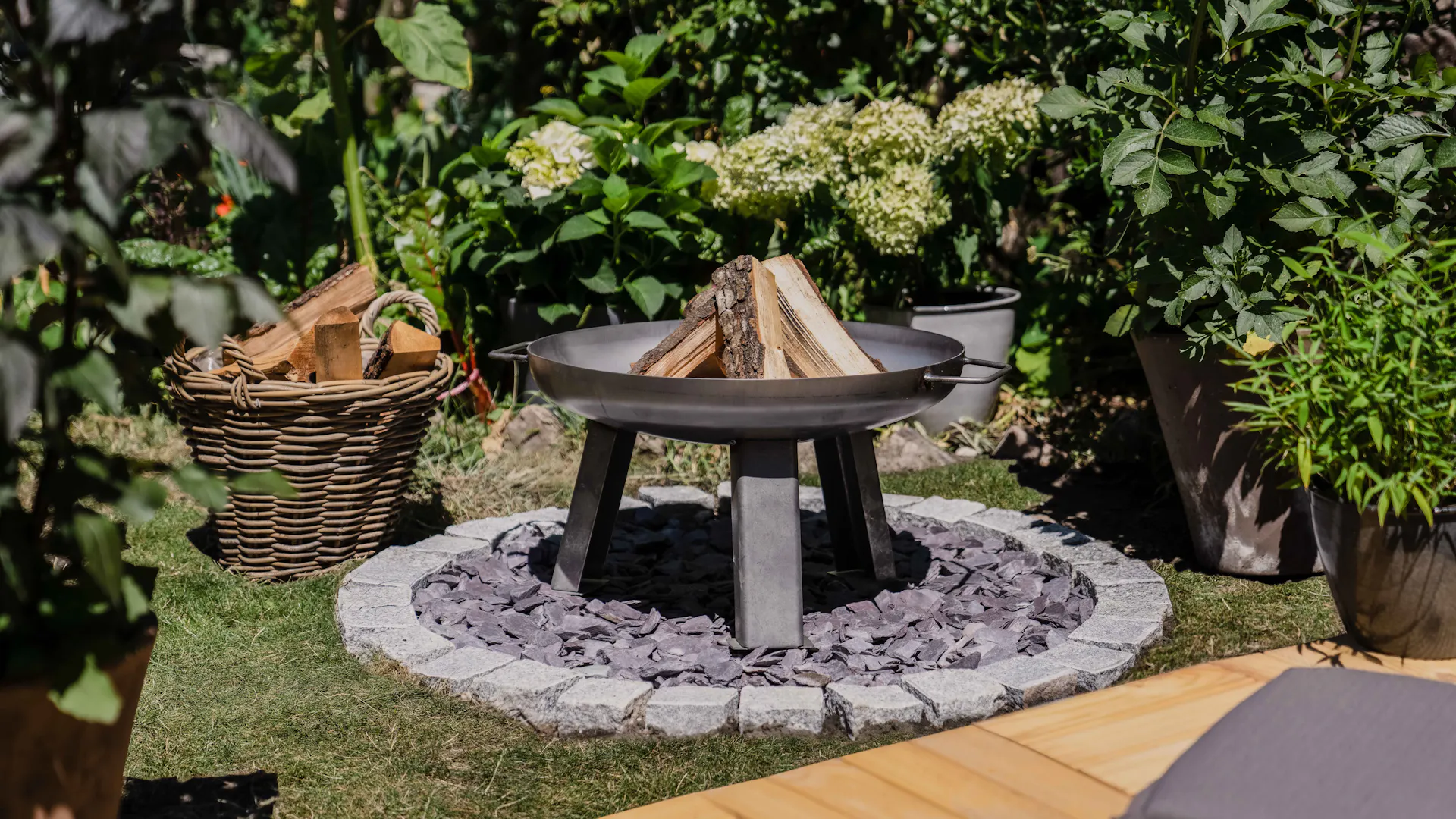 Feuerstelle neben Korb mit Feuerholz im Garten