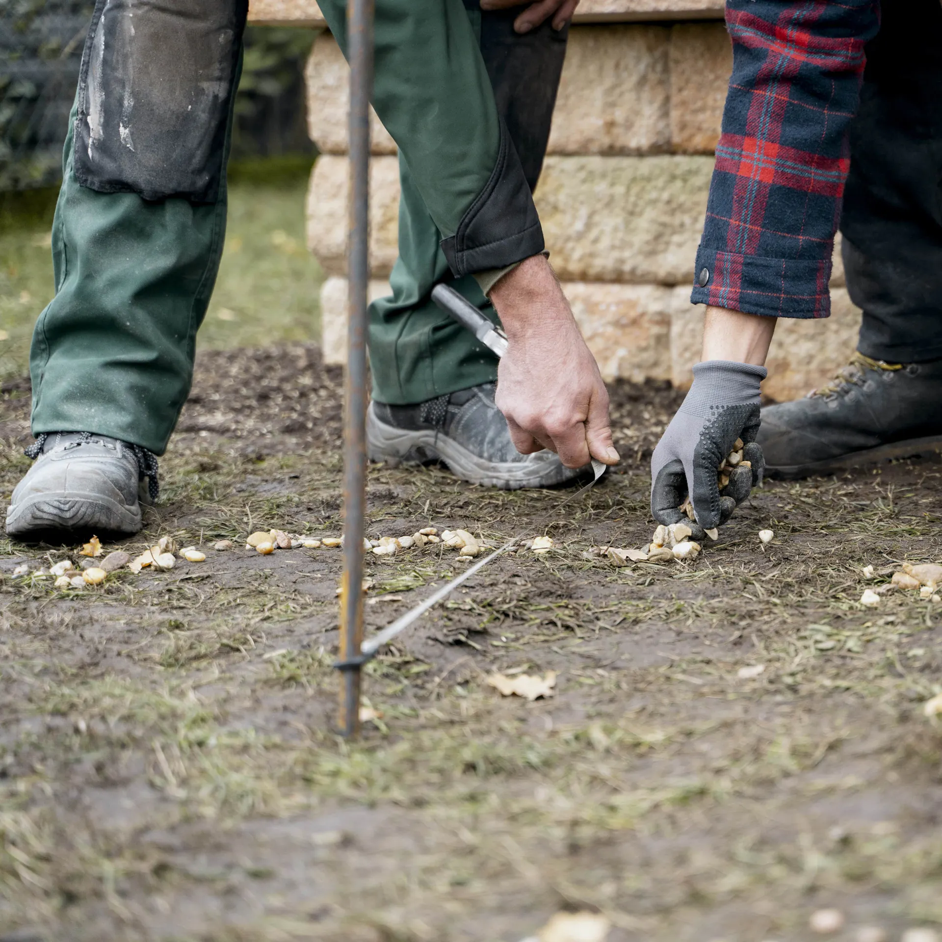 Heimwerker verteilen Kieselsteine als runden Kreis auf Gartenboden für den Bau einer Feuerstelle.