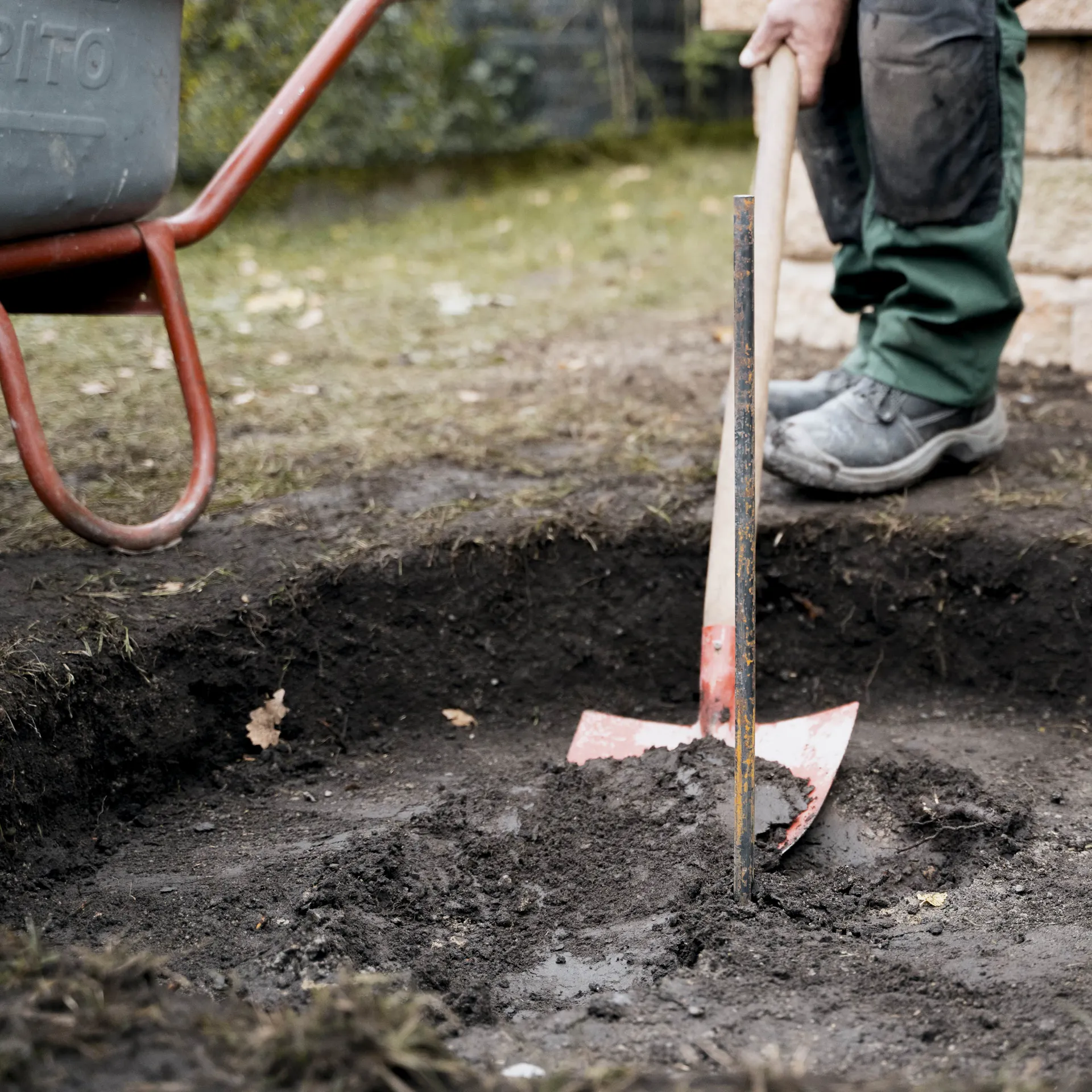 Heimwerker schachtet runde Fläche im Garten mit Schaufel aus.