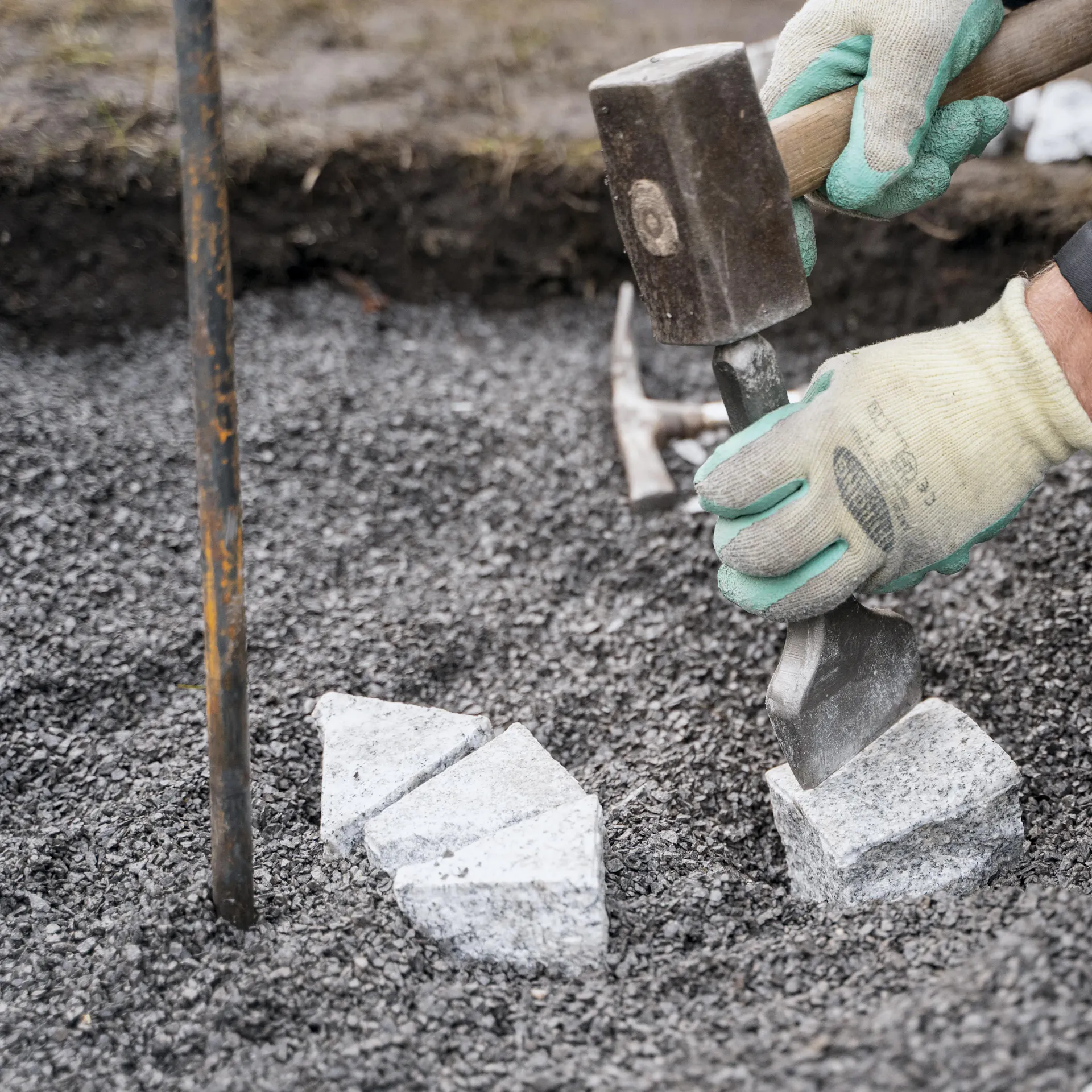Heimwerker schlägt Pflastersteine mit Hammer und Meißel in Dreiecke.