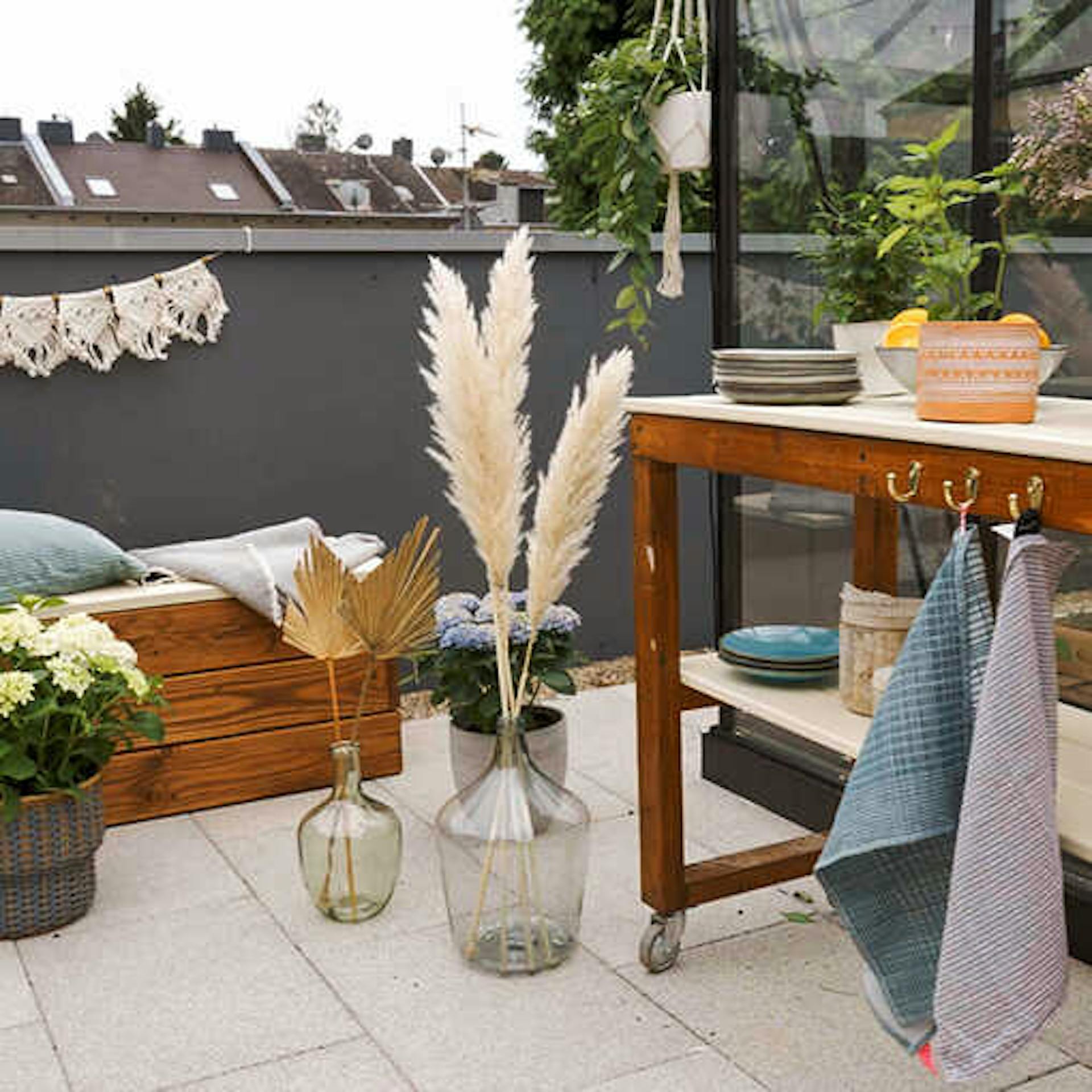 Bank Alfred und Servierwagen Sophie stehen auf einer mit Vasen und Trockenblumen geschmückten Dachterrasse.