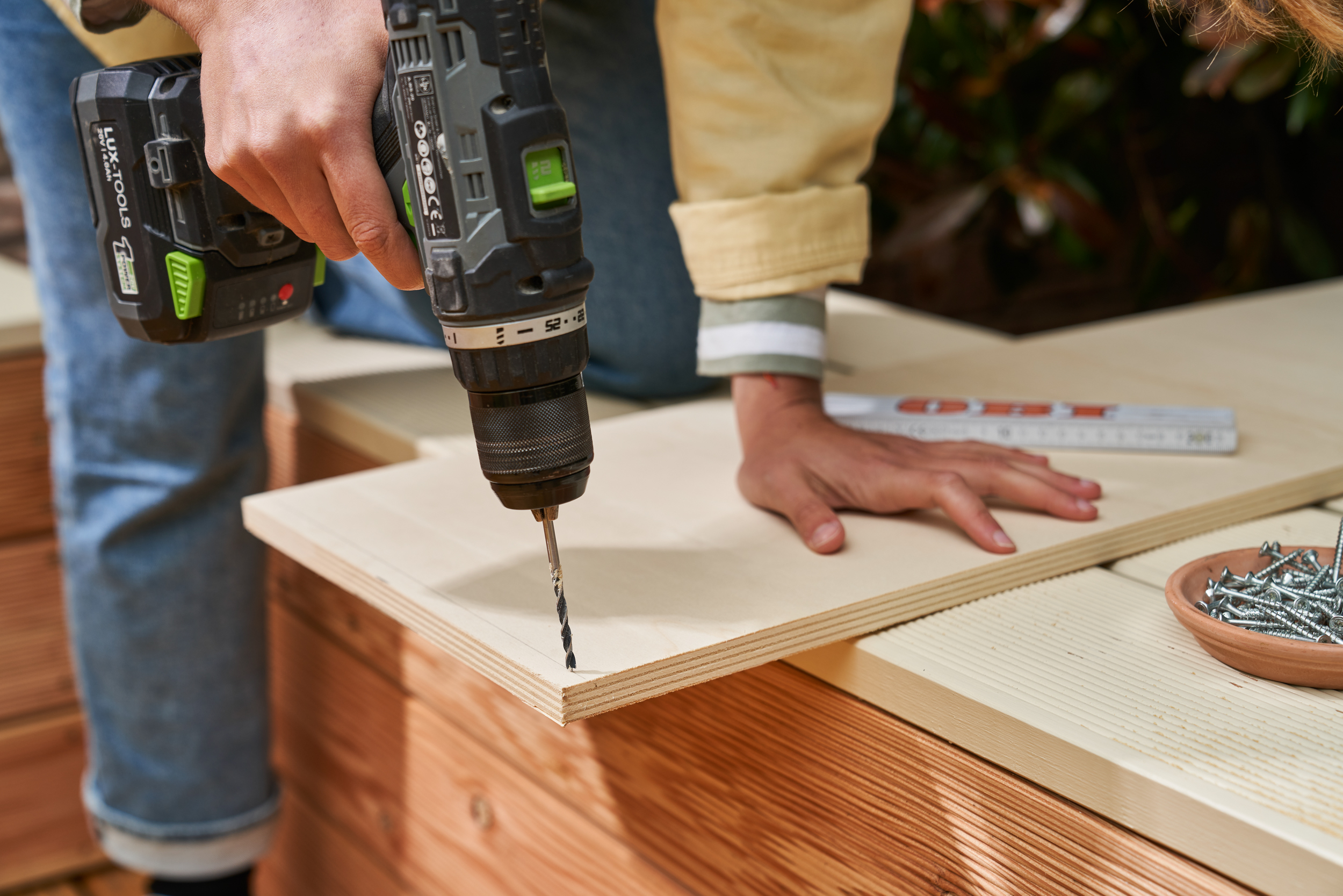 A barkácsoló előfúrja a megjelölt lyukakat az építőelemben a lábfürdő medencéjéhez.
