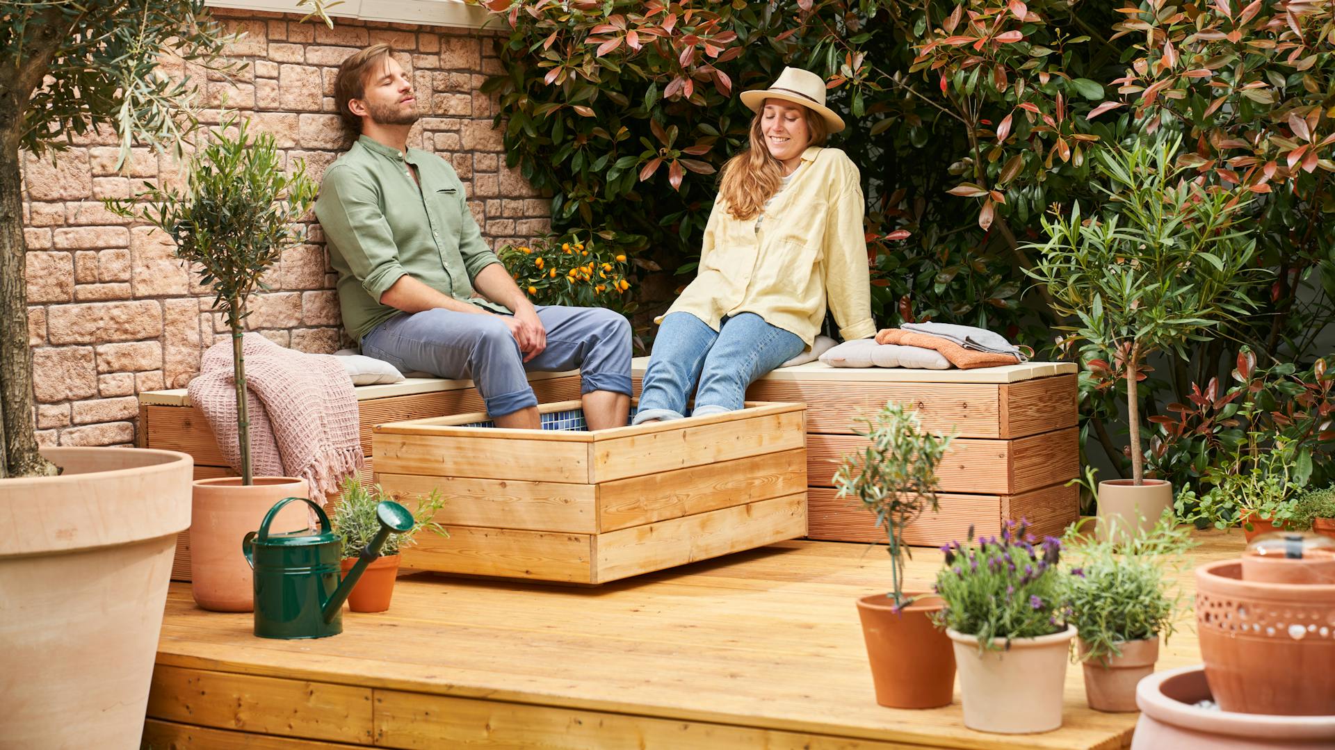 Paar sitzt auf Bänken in Entspannungecke, die Füße im selbstgebauten Fußbad