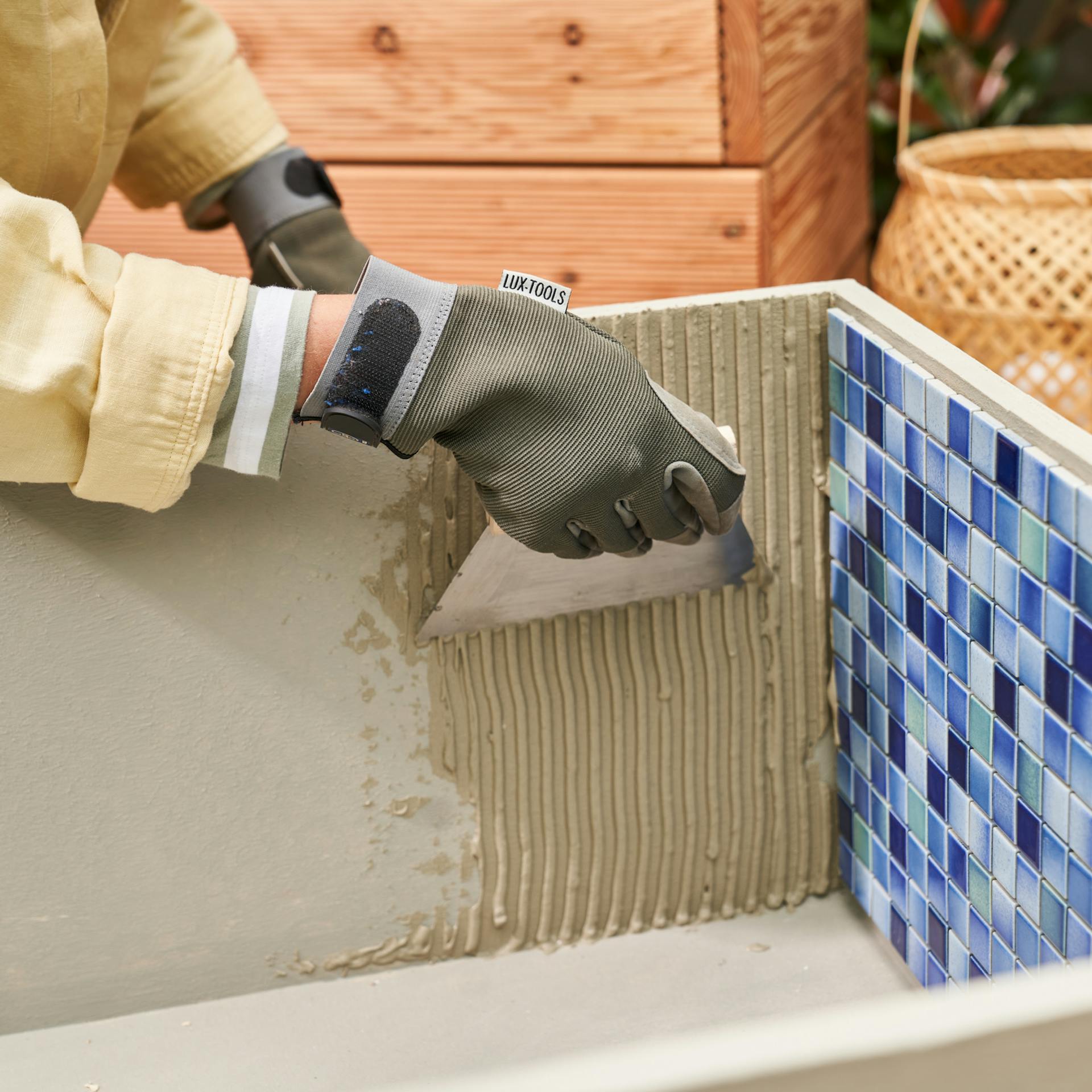 Heimwerkerin verteilt Fliesenkleber auf der Innenseite des Fußbeckens, in dem bereits auf einer Seite Fliesen befestigt sind.