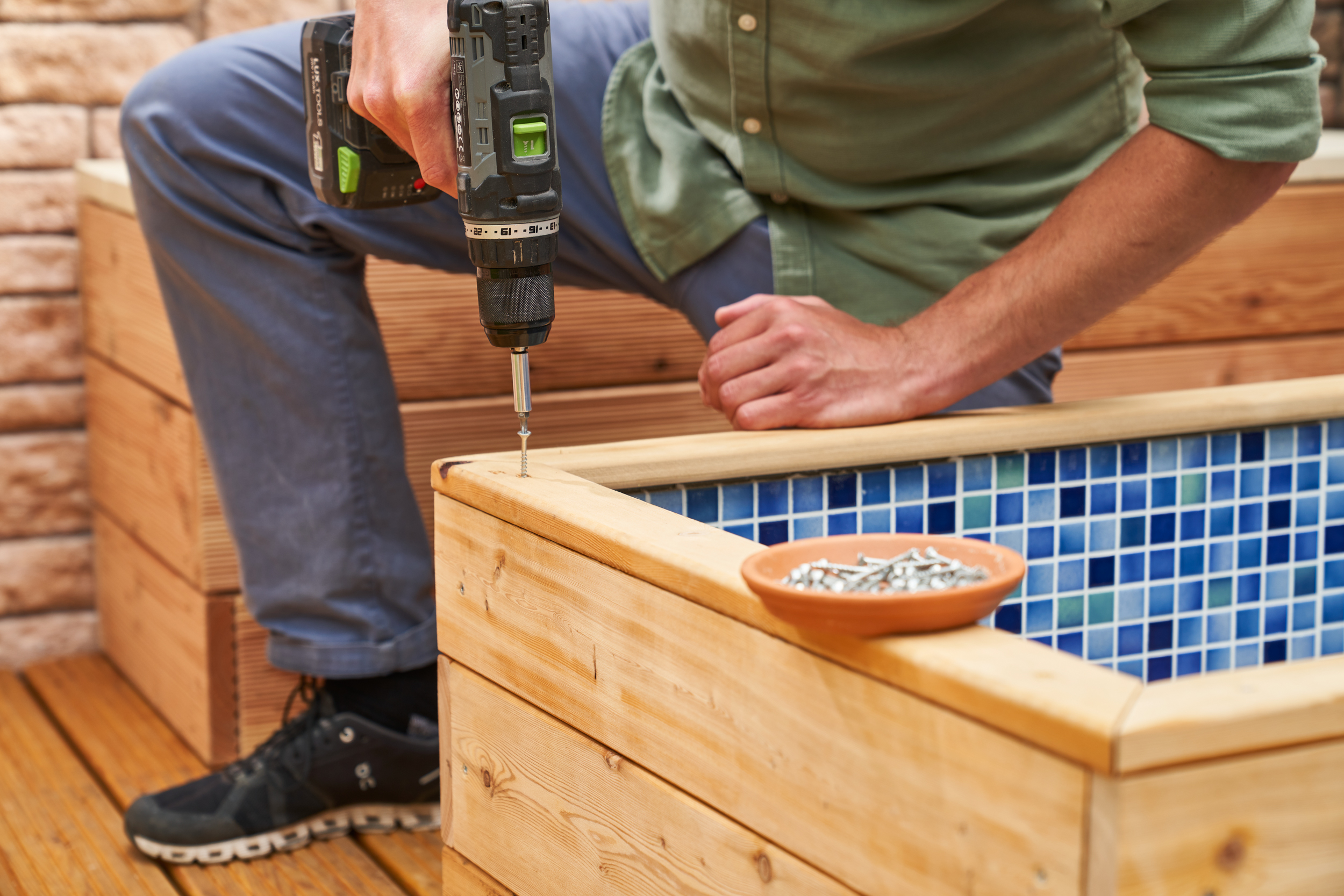 A barkácsoló a lábfürdő fapárkányát csavarozza.