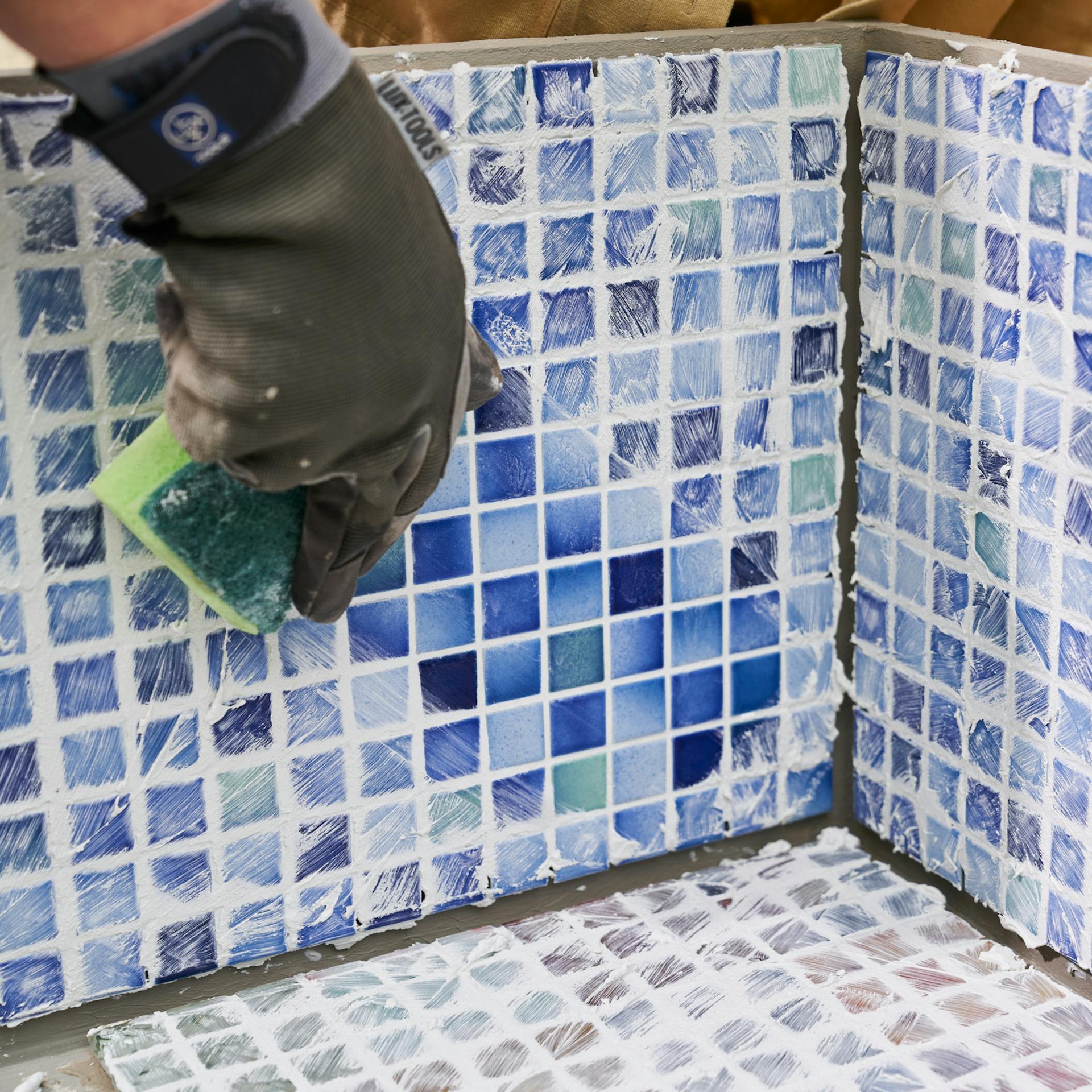 Heimwerkerin trägt überschüssige Fugenmasse mit einem Schwamm ab.