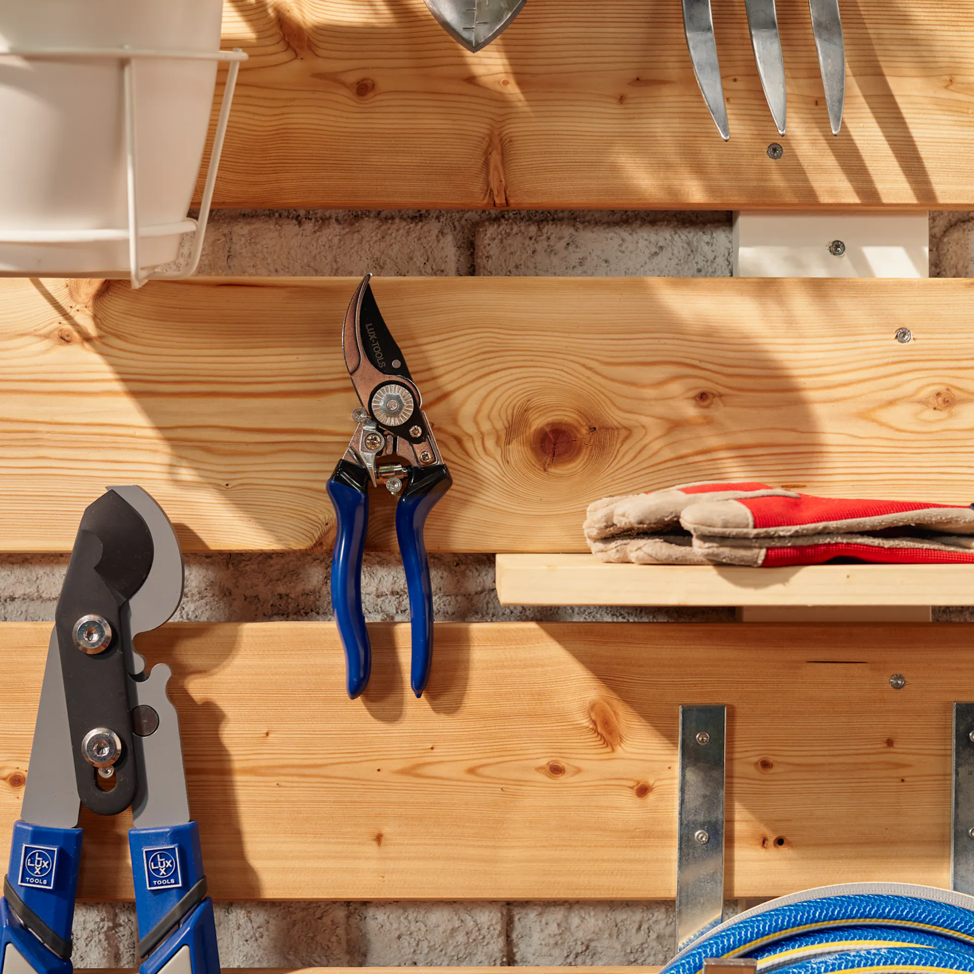 DIY Garden-Organizer, an dem ein paar Utensilien hängen, unter anderem eine Zange, Handschuhe und ein Gartenschlauch.