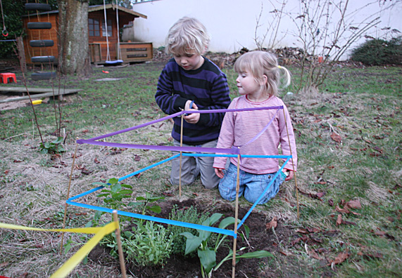 Kinder sperren ein Kinderbeet mit bunten Bändern ab.