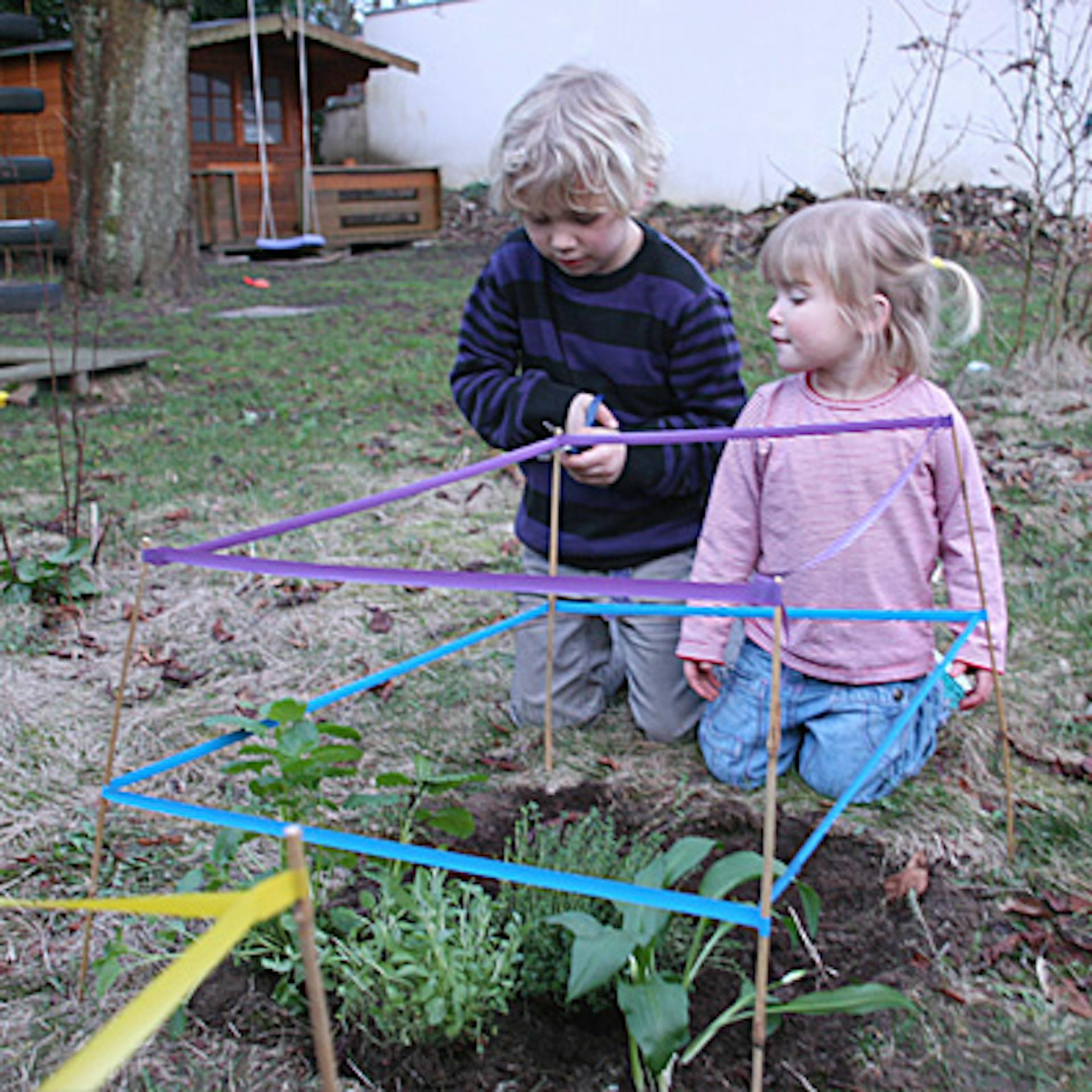 Kinder sperren ein Kinderbeet mit bunten Bändern ab.