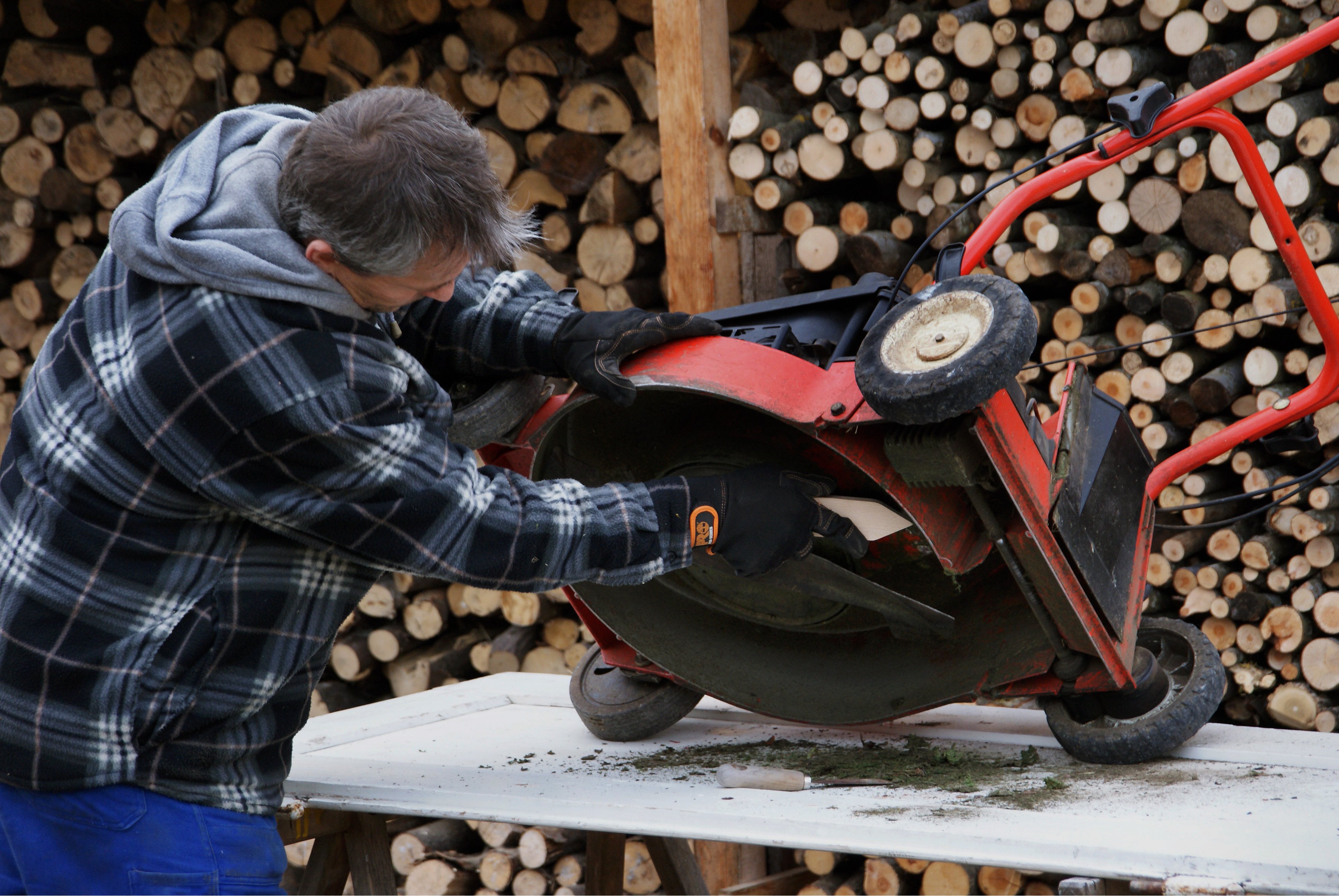 Ein Mann baut das Rasenmähermesser bei einem Rasenmäher aus.