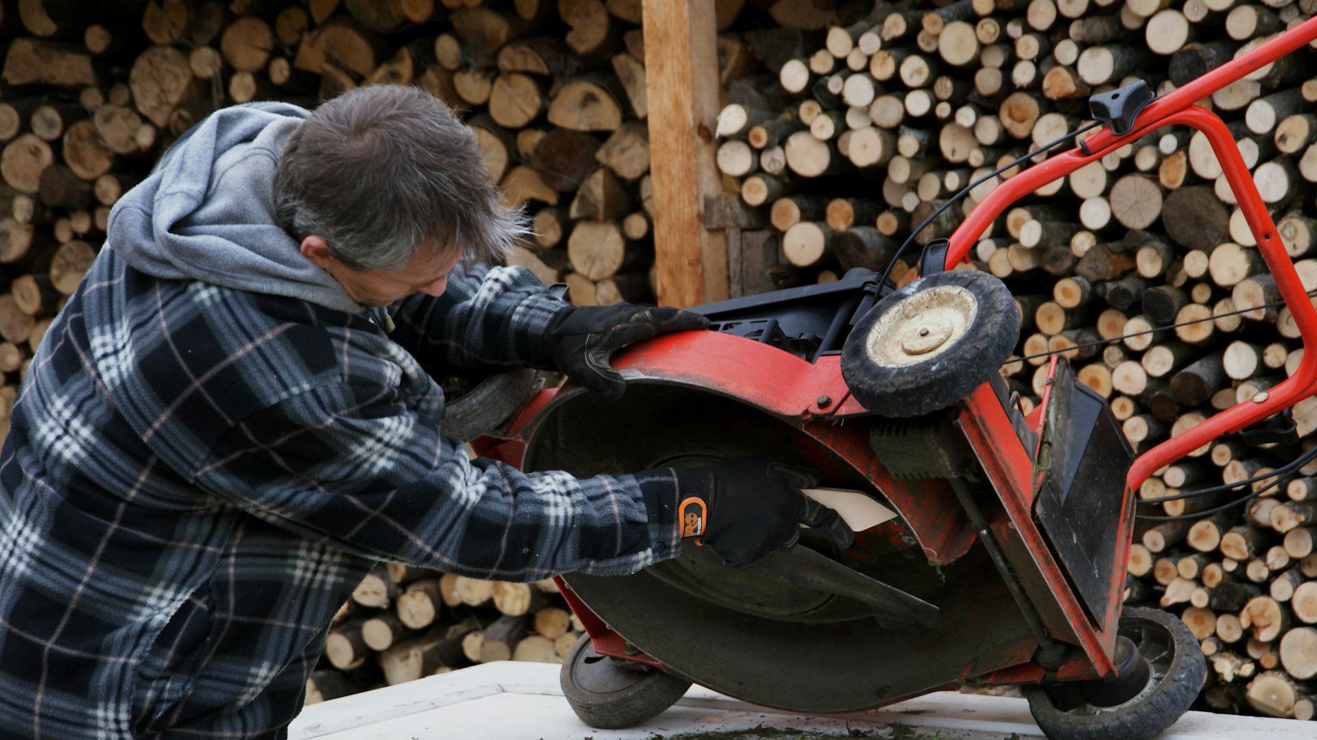 Ein Mann säubert einen Rasenmäher von unten.