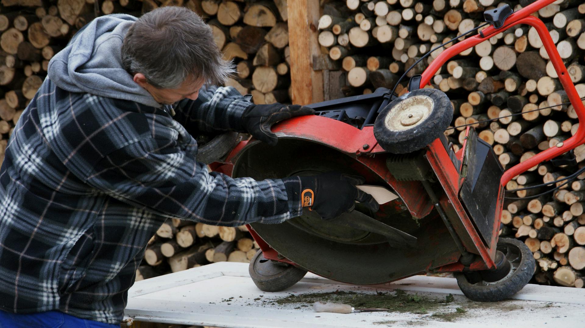 Ein Mann baut das Rasenmähermesser bei einem Rasenmäher aus.