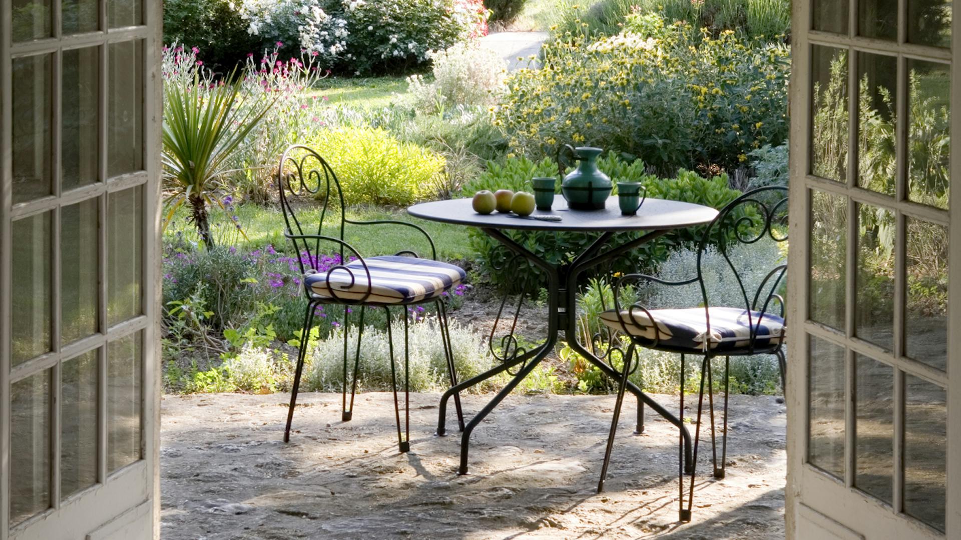 Ein schwarzer Metall-Gartentisch und zwei Gartenstühle aus Metall stehen im Garten.