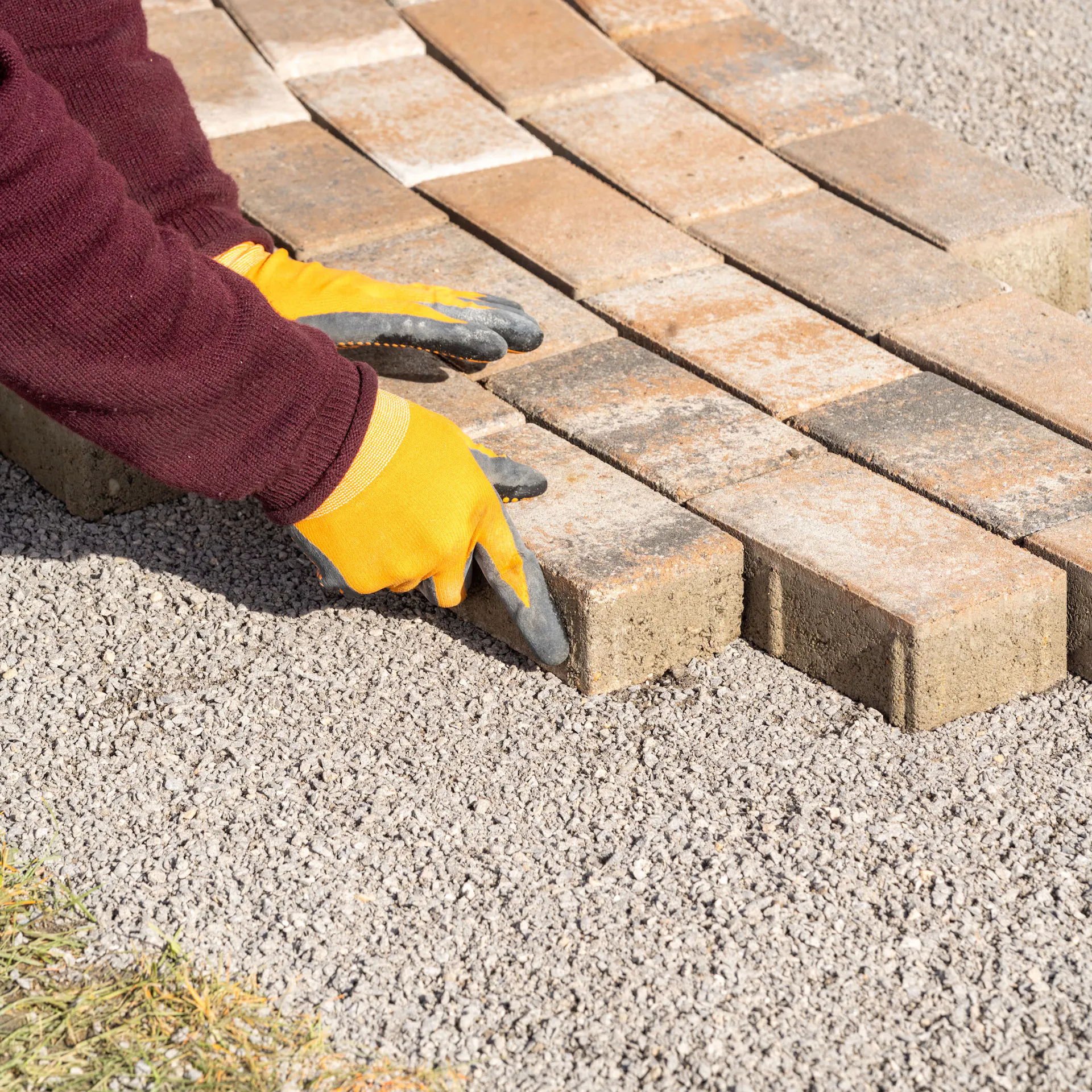 Ruce pokládající dlažební kostku na štěrk