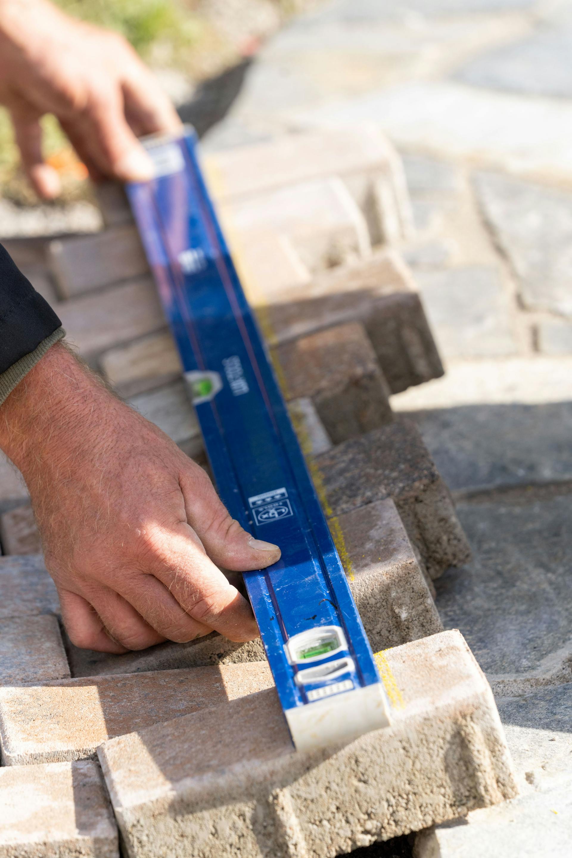 Mani tengono una livella a bolla contro diverse pietre per selciati