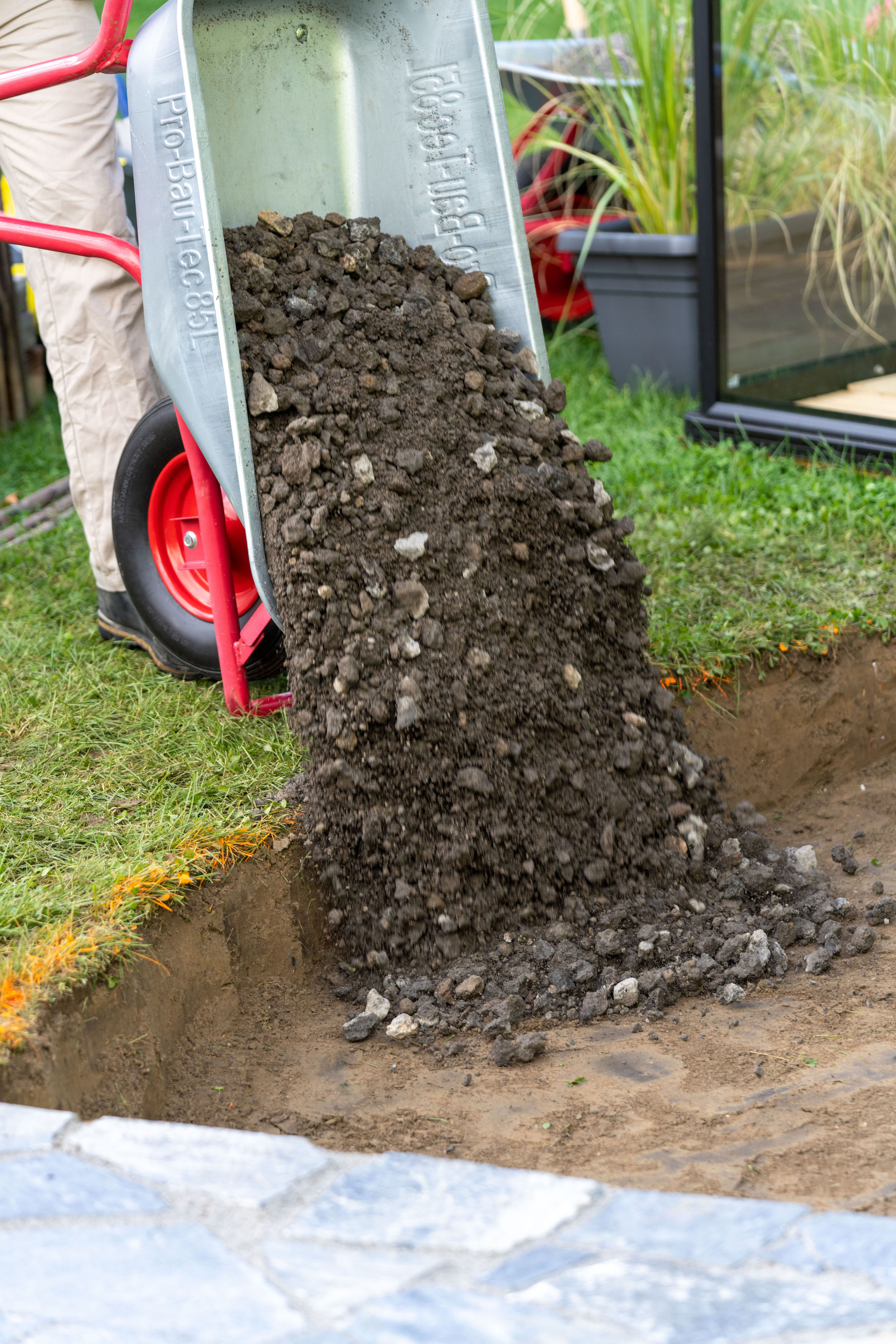 Schotter wird mit einer Schubkarre in ein Erdloch geschüttet