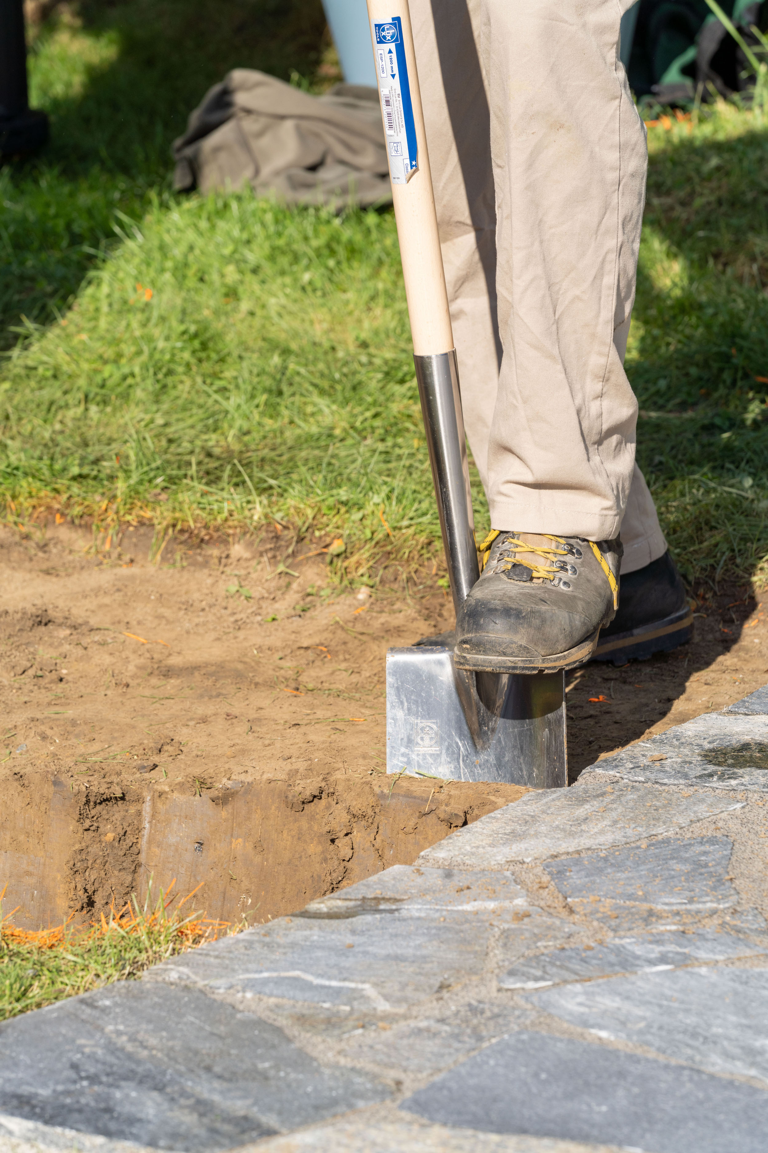 Mann steht mit dem Fuß auf einem Spaten, der in der Erde steckt