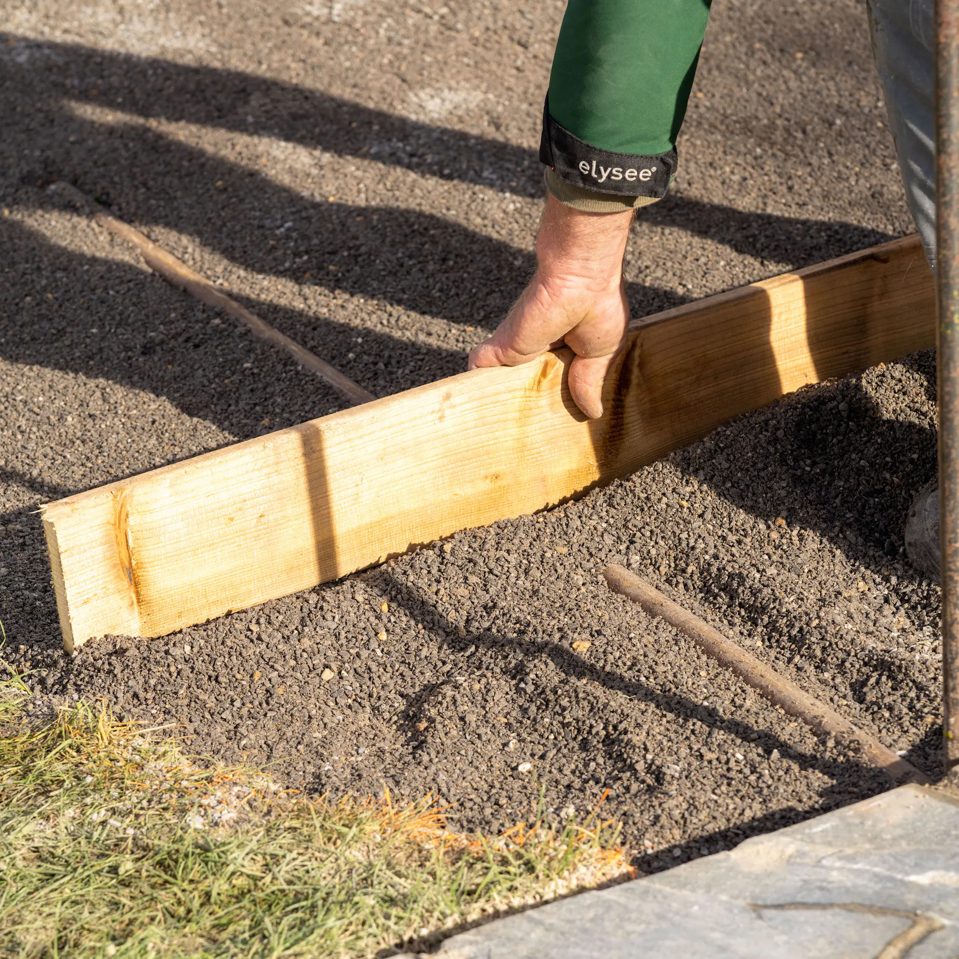 Jednou rukou drží dřevěné prkno na vrstvě štěpky.