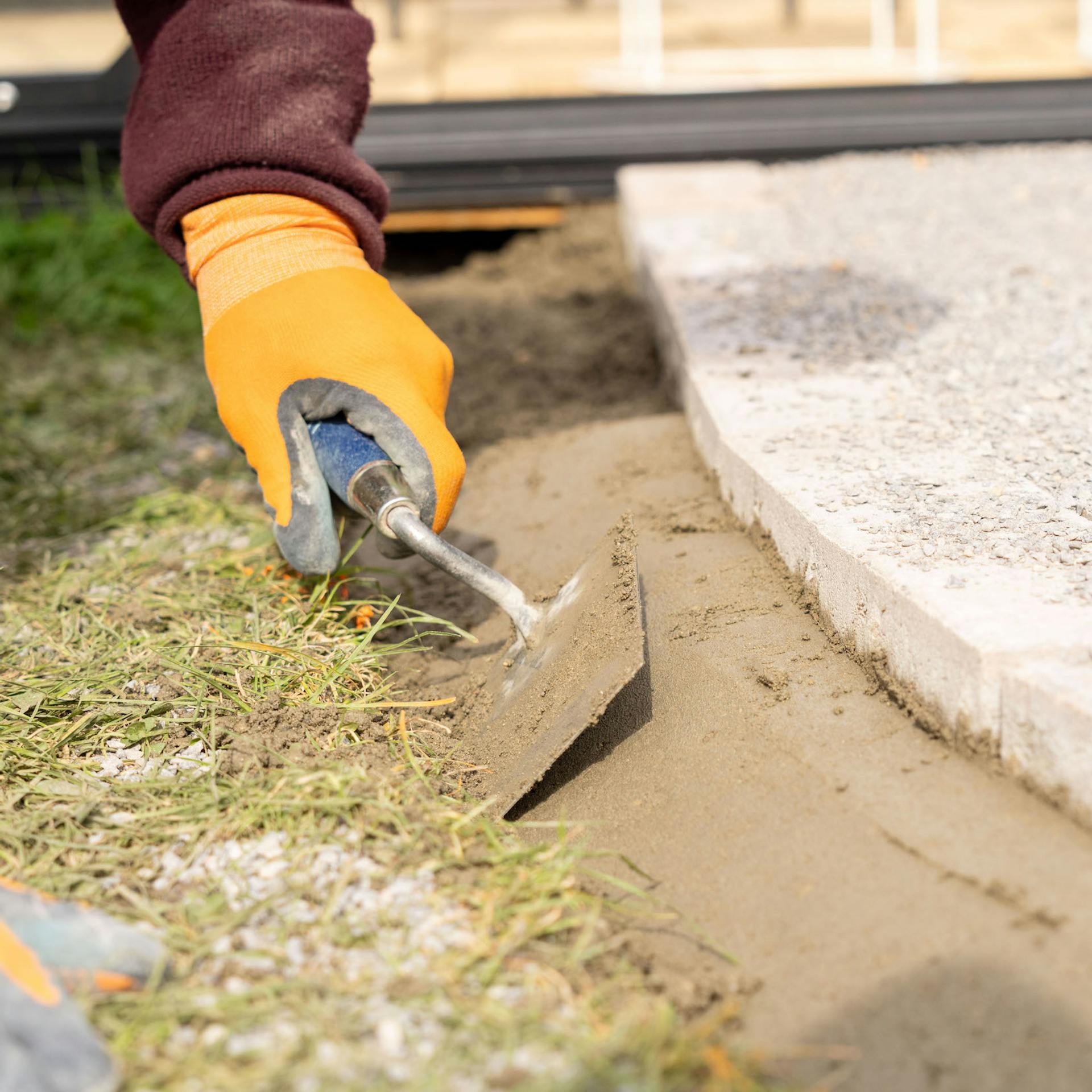 Eine Hand verteilt Gartenbeton am Rand eines Pflasterwegs