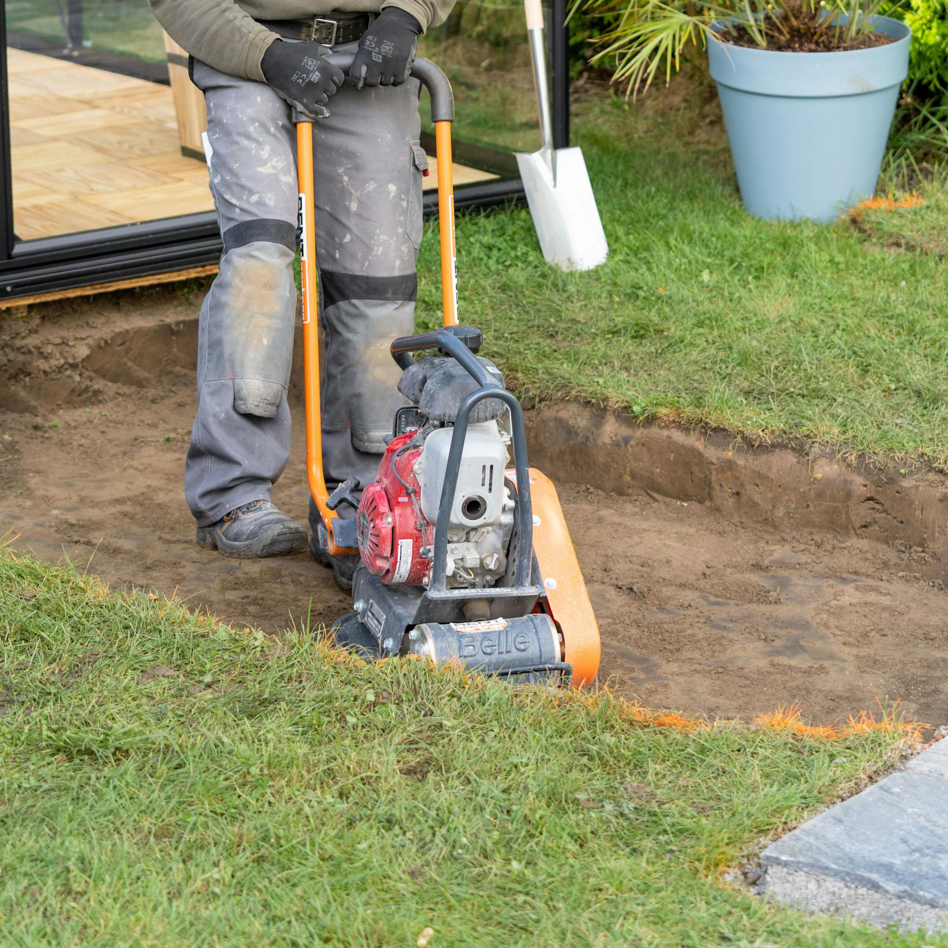 Ein Handwerker fährt mit einer Rüttelplatte über eine ausgehobene Fläche