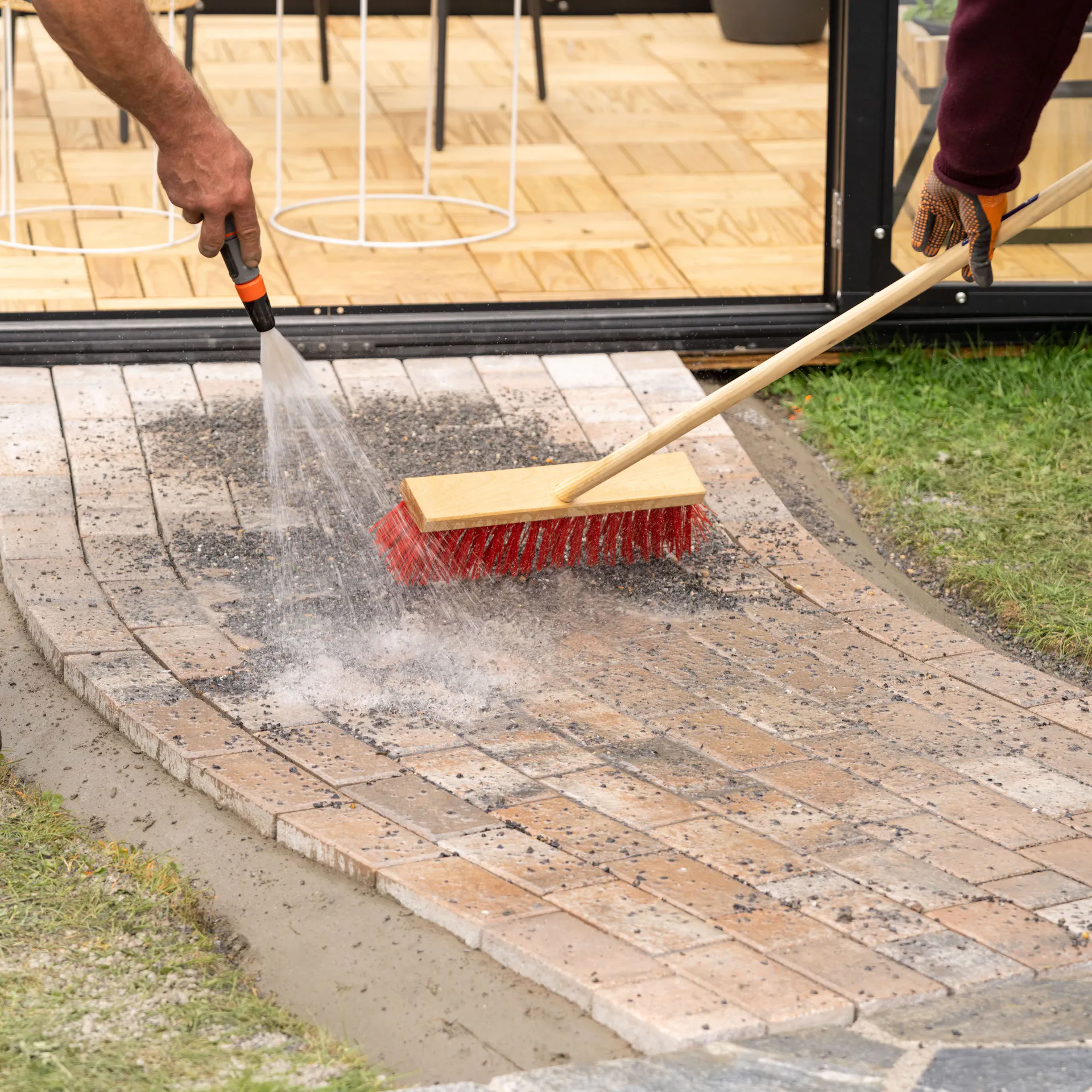 Dlážděná cesta s posypem se zalévá zahradní hadicí.