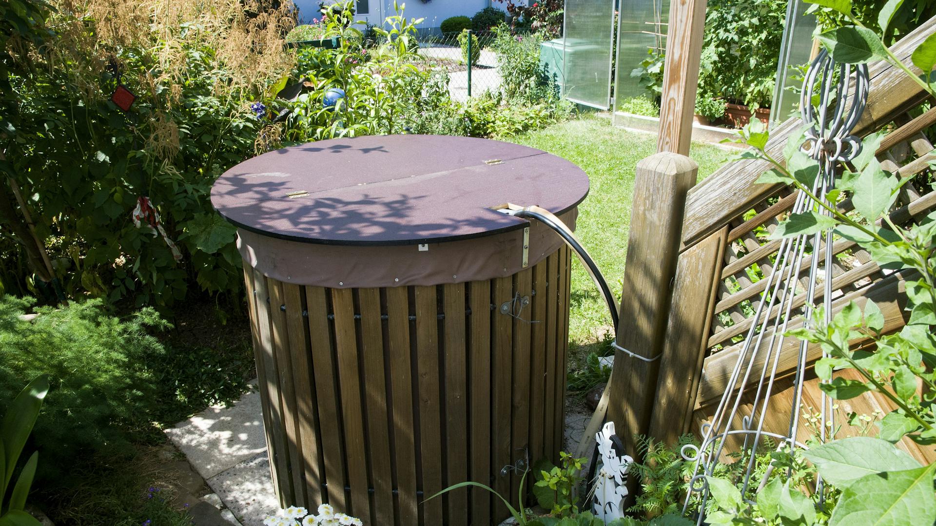 Eine braune Holz-Regentonne steht im Garten.