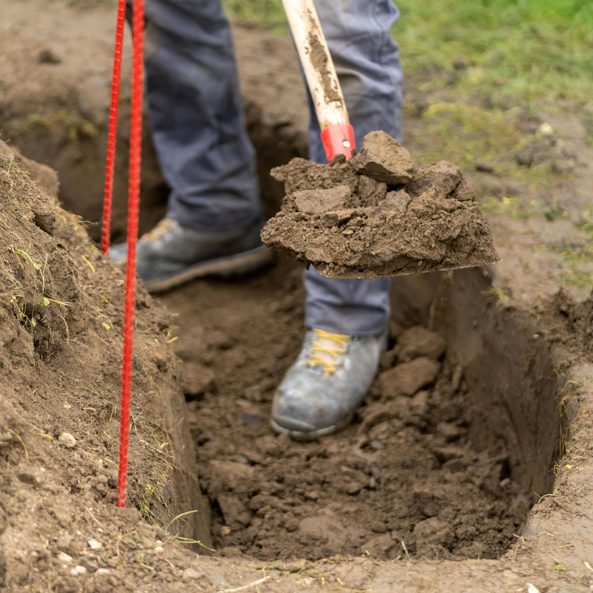 Person hebt mit einem Spaten einen Graben aus.