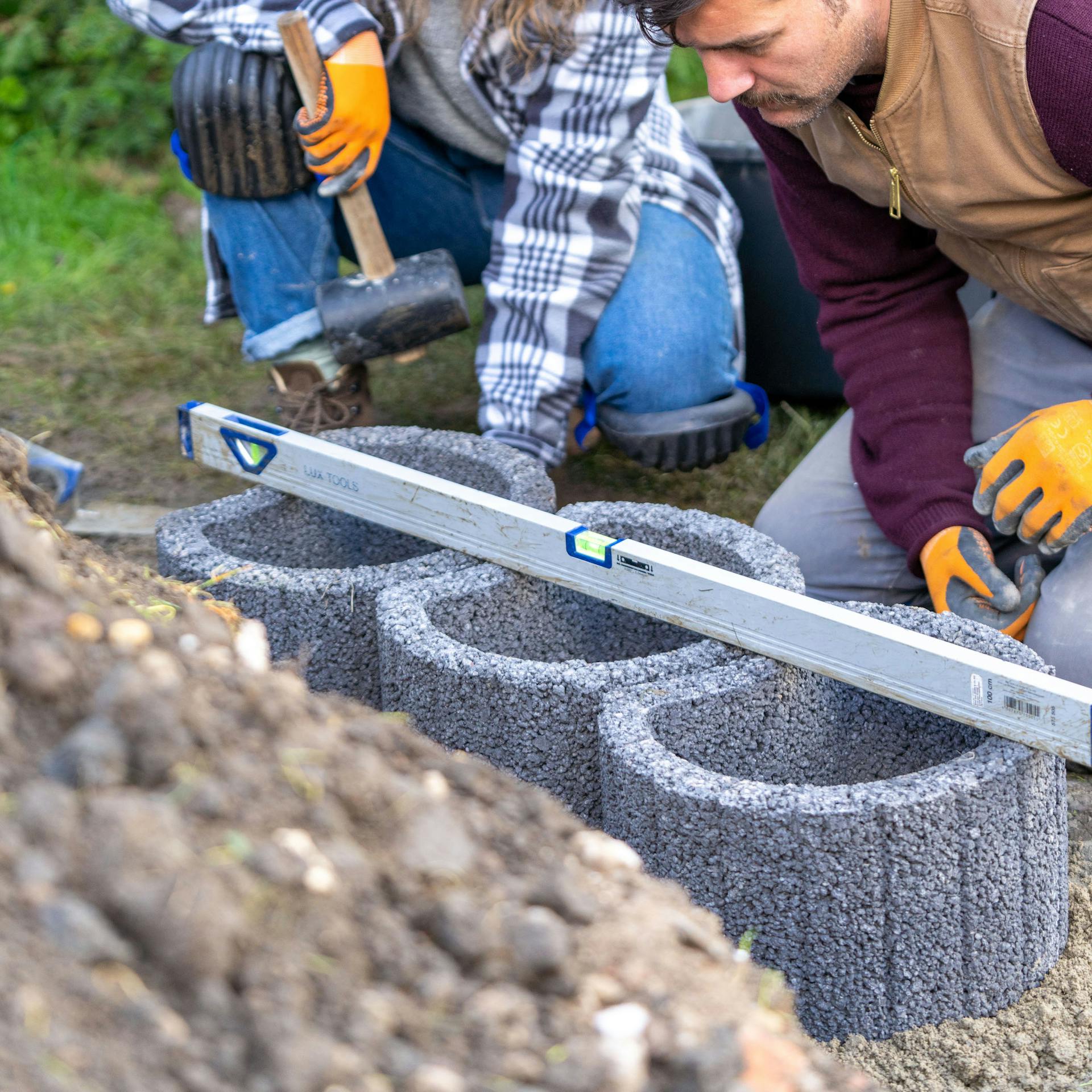 Drei Pflanzsteine stehen nebeneinander und eine Wasserwaage liegt längs darauf.