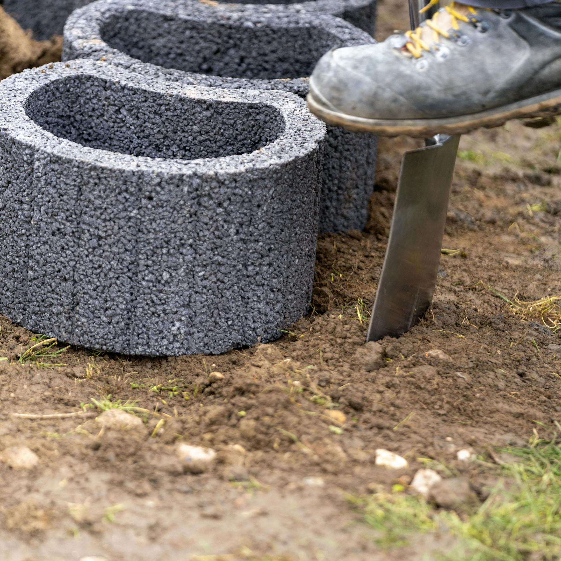 Person sticht den Boden rund um Pflanzsteine an.