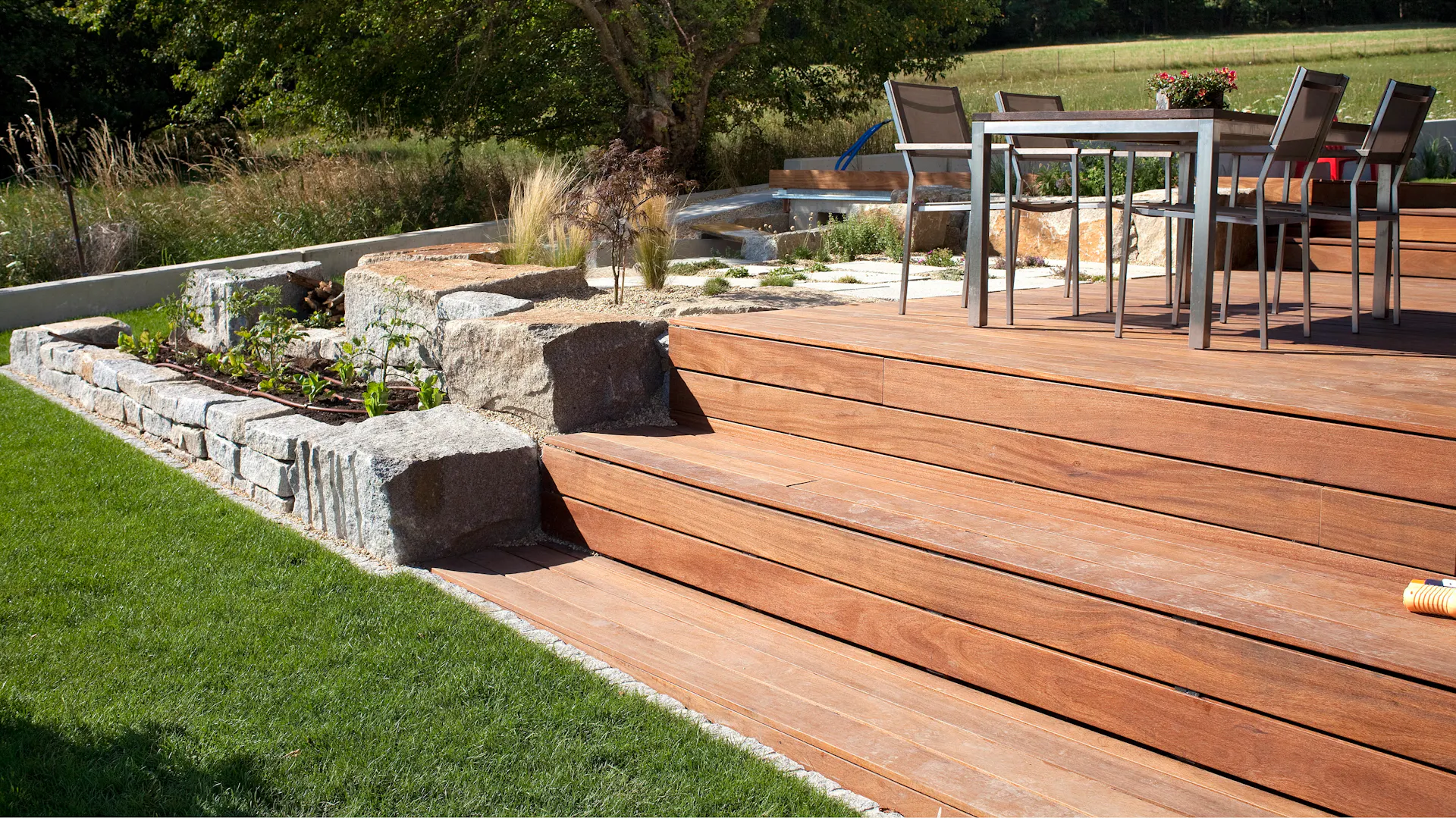 Holzterrasse mit bepflanztem Hanggarten und Gartengarnitur